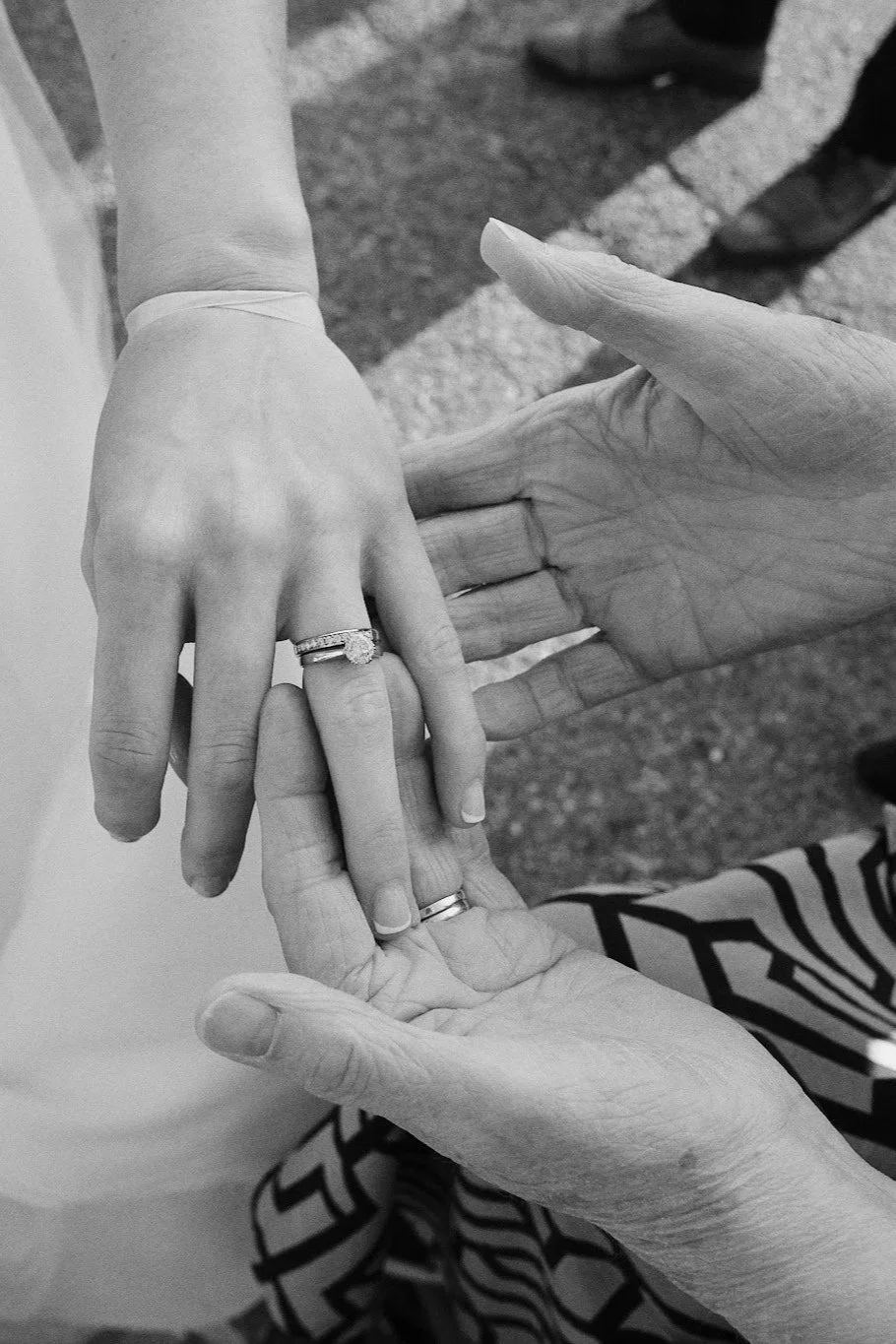 Tre personer visar sina händer, två av dem bär ringar, och håller varandra i ett gemensamt handslag, troligen symboliserande kärlek eller äktenskap. Bilden är i svartvitt.