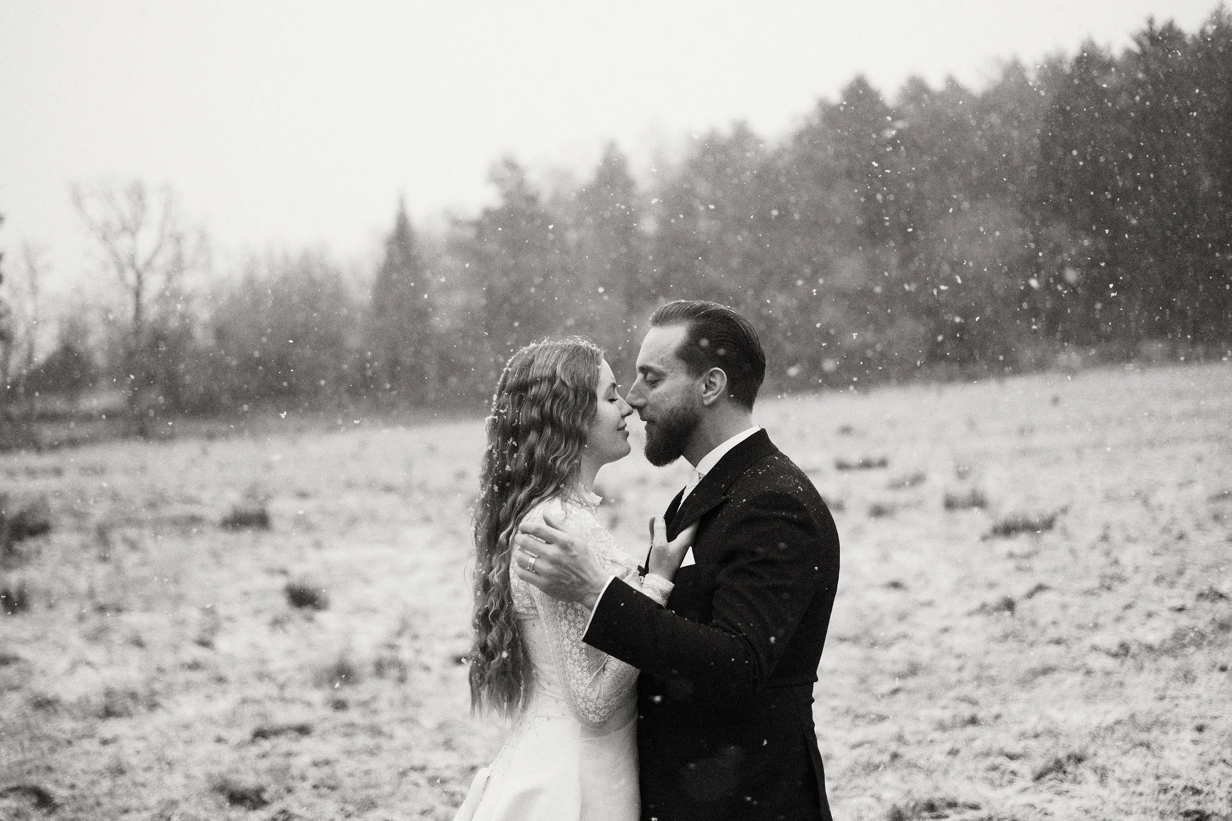 Brudpar står tillsammans i snöfall under ett katolskt vinterbröllop