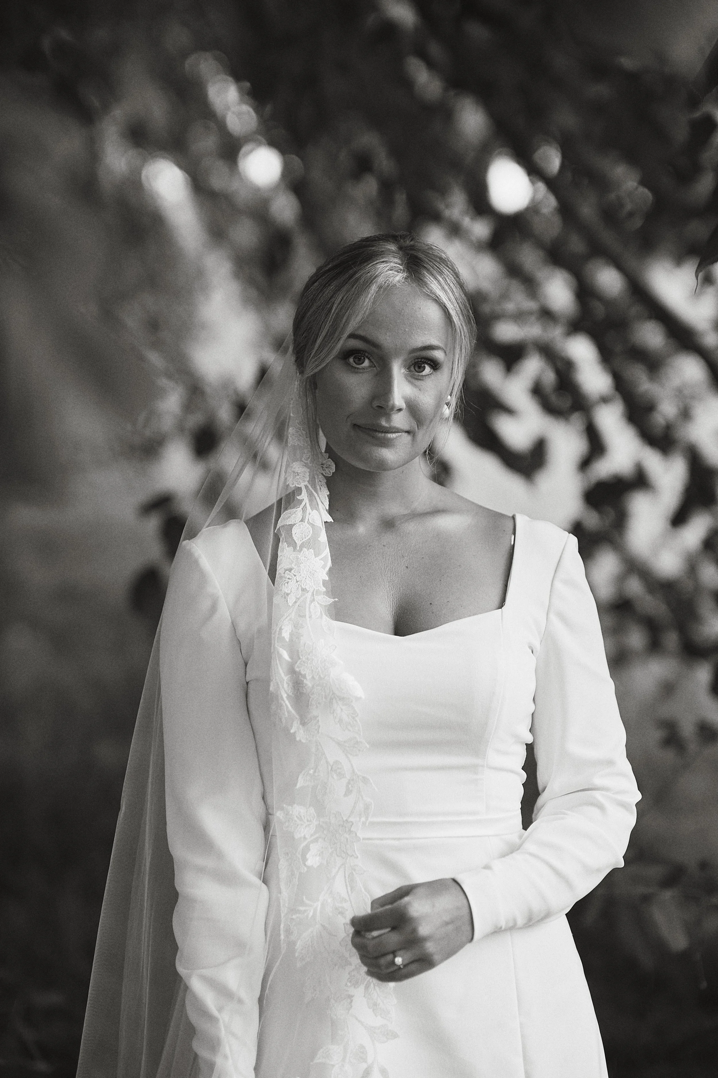 En brud i vit brudklänning med slöja, stående utomhus, svartvitt foto.