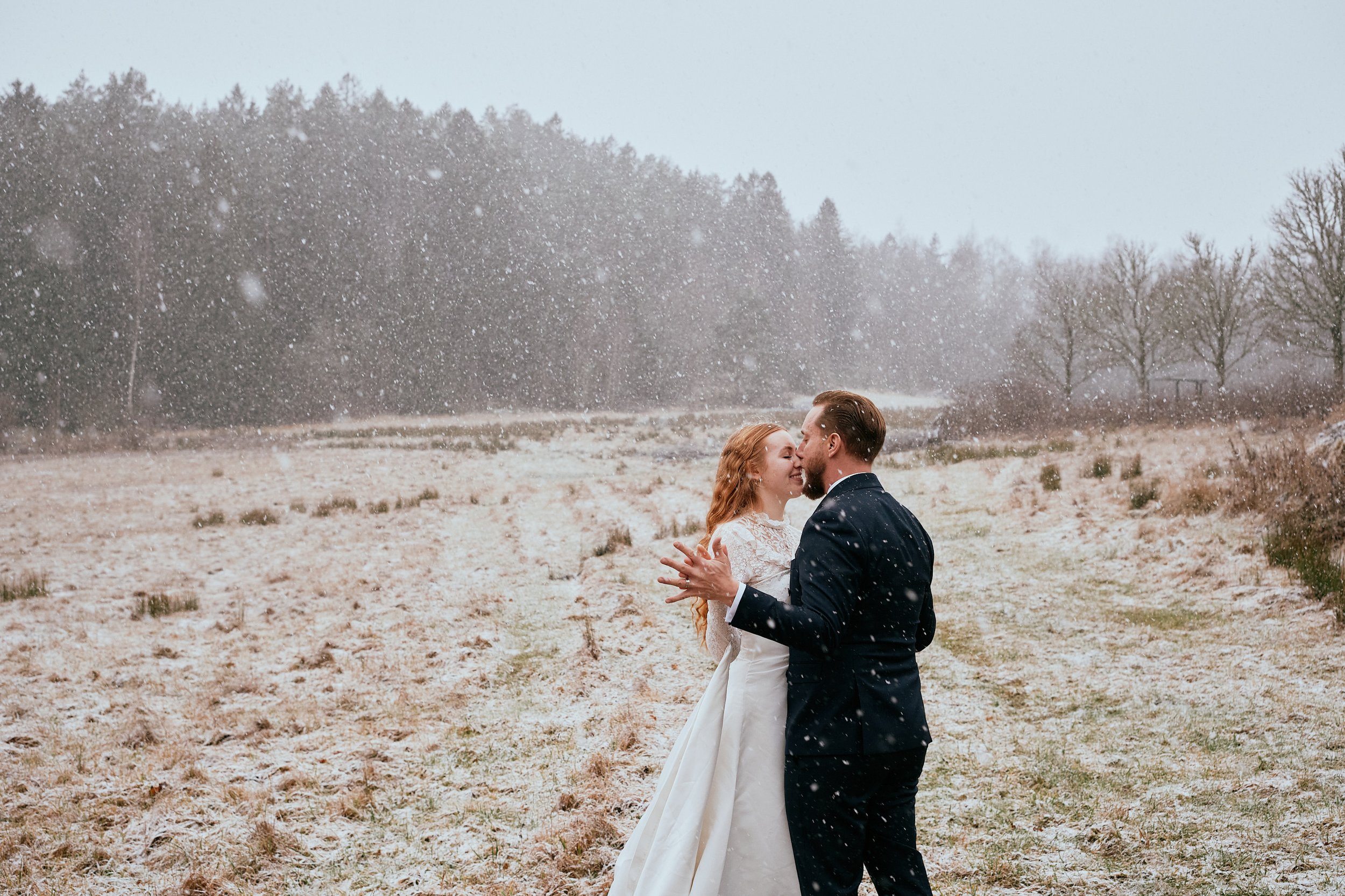 Brudpar i snöfall under ett katolskt vinterbröllop, fångat i ett stilla och närvarande ögonblick