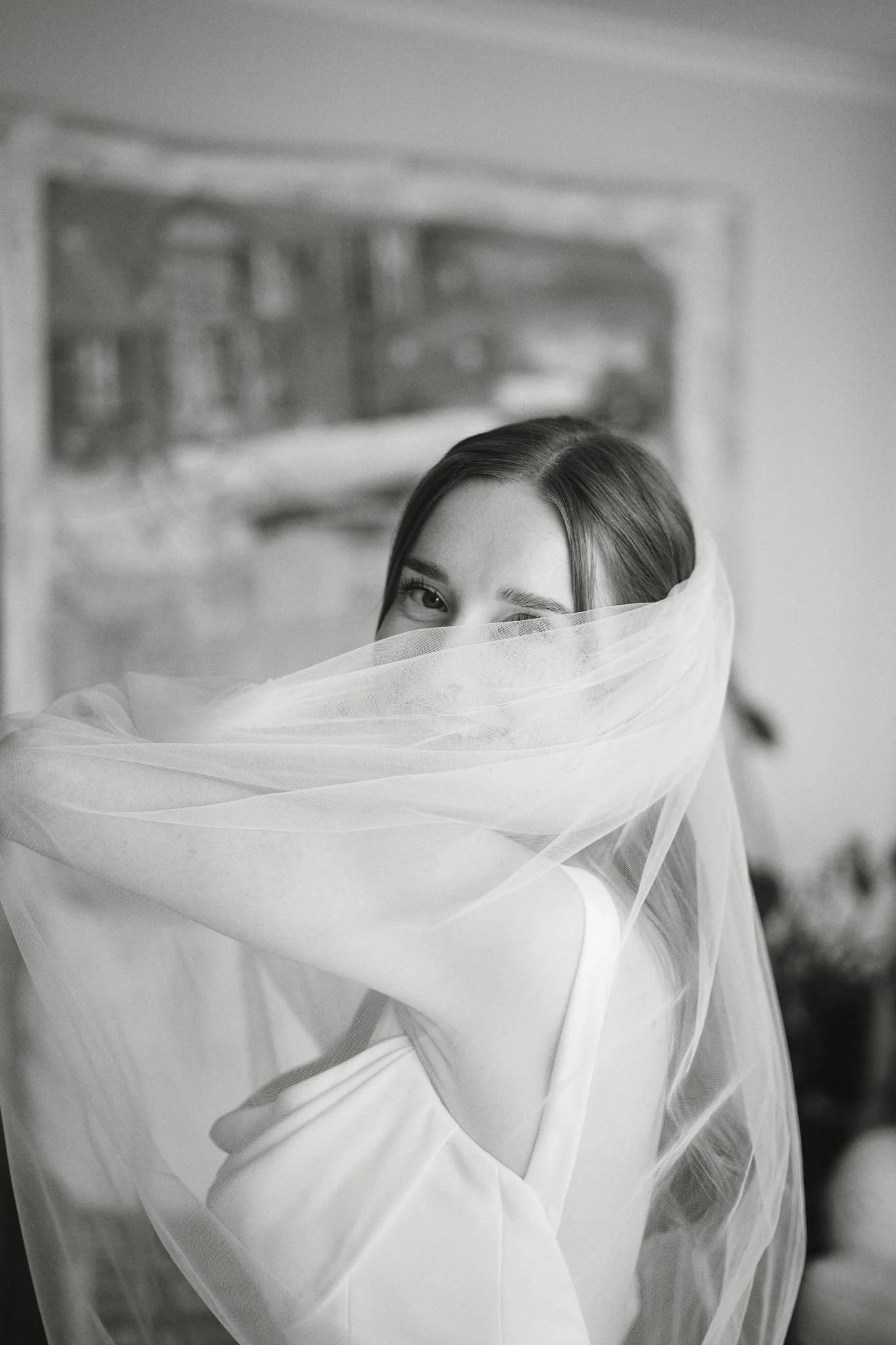 Svartvit bild av en kvinna som bär en tunn, transparent slöja som täcker halva ansiktet, synlig öga, bakgrund med konstnärlig målning.