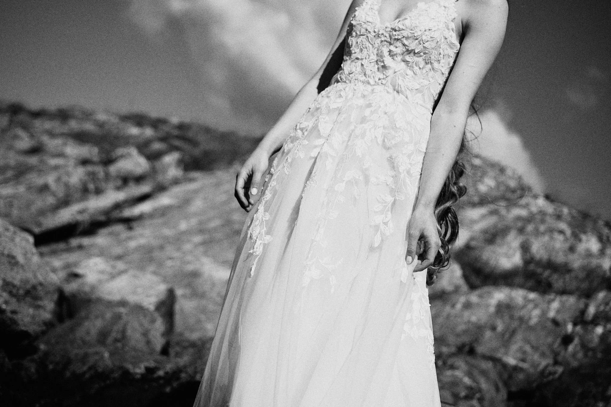 En brud i bröllopsklänning står utomhus i ett stenigt landskap