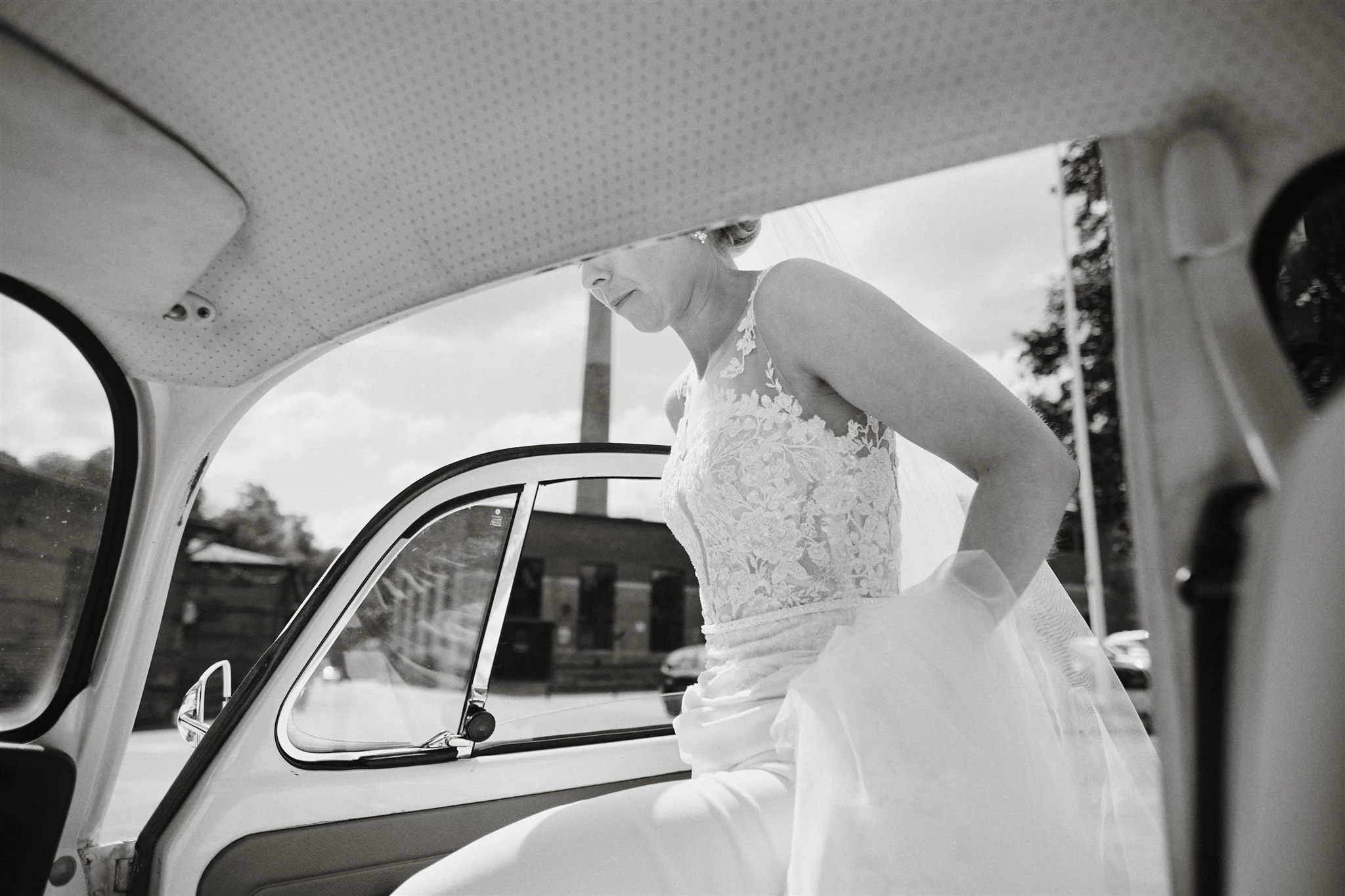 Brud kliver in i bilen inför vigseln, fotograferad i naturligt ljus
