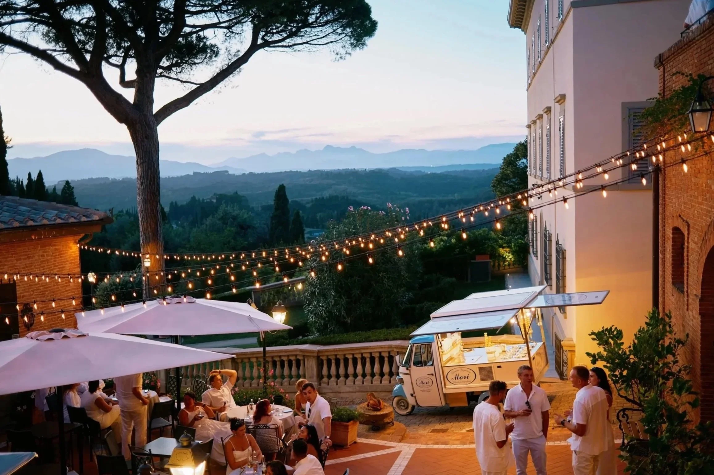 Stämningsfull bröllopskväll i Toscana med ljusslingor, gäster och utsikt över kullarna