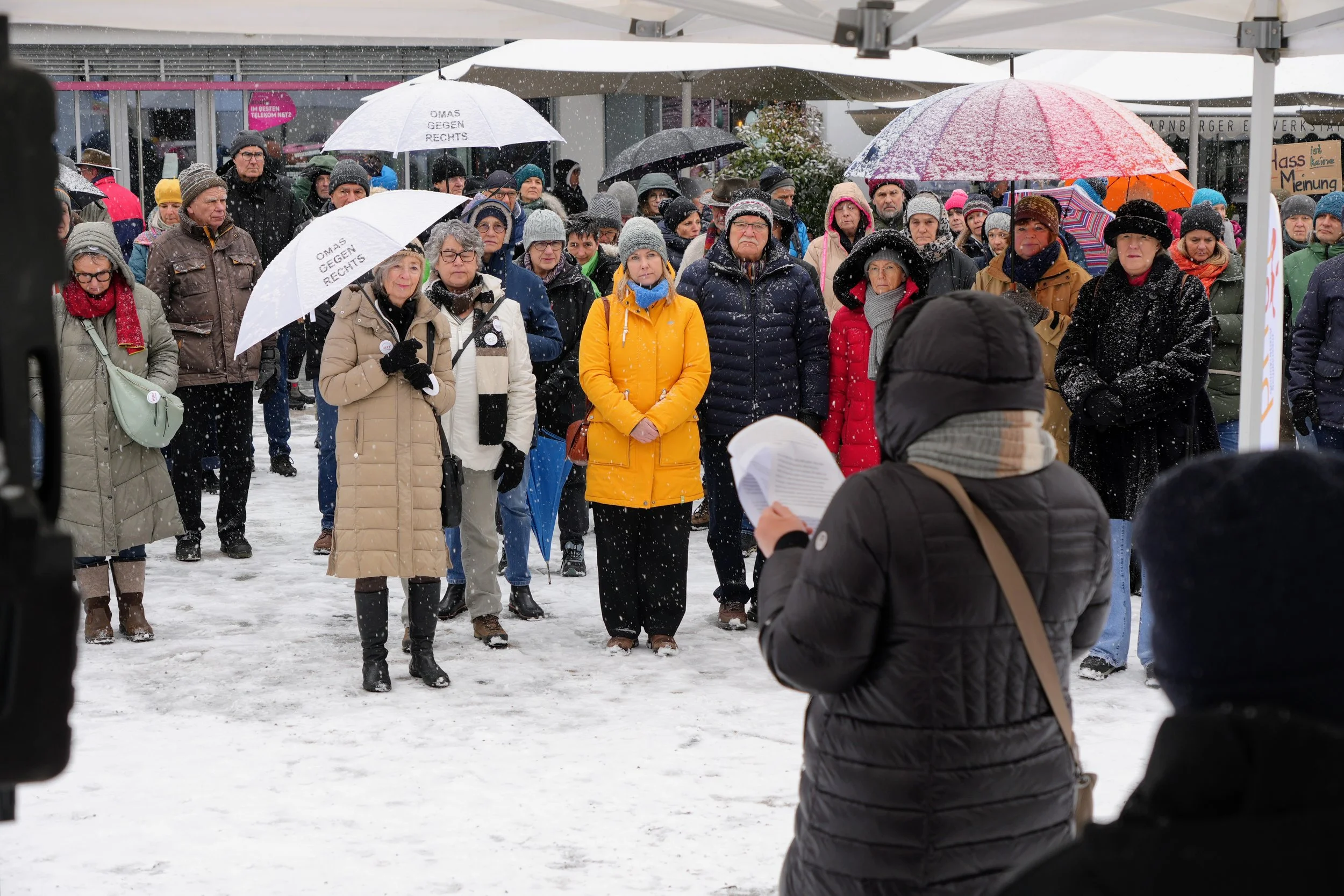 Menschen versammeln sich im Schnee, einige tragen Regenschirme, bei einer Demonstration oder Kundgebung.