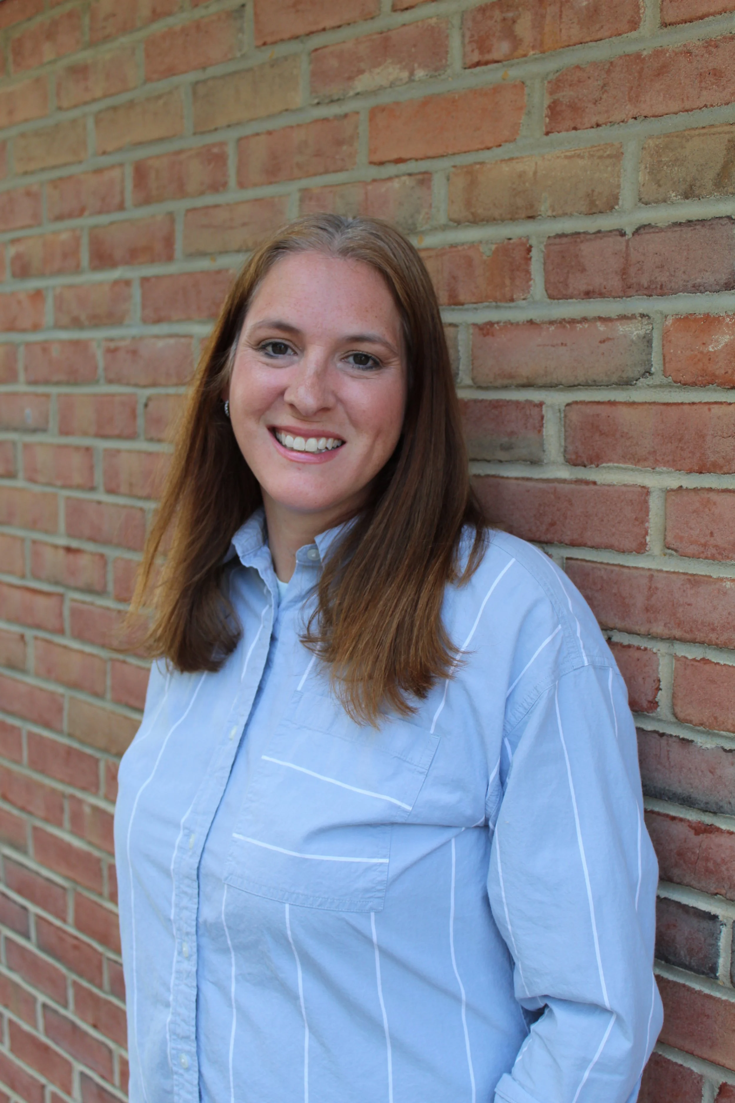 Headshot of Samantha Page, a woman with long brown hair, smiling, wearing a blue collared shirt.