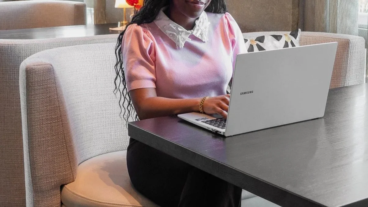 Vrouw zit aan een tafel met een laptop in een woonkamer.
