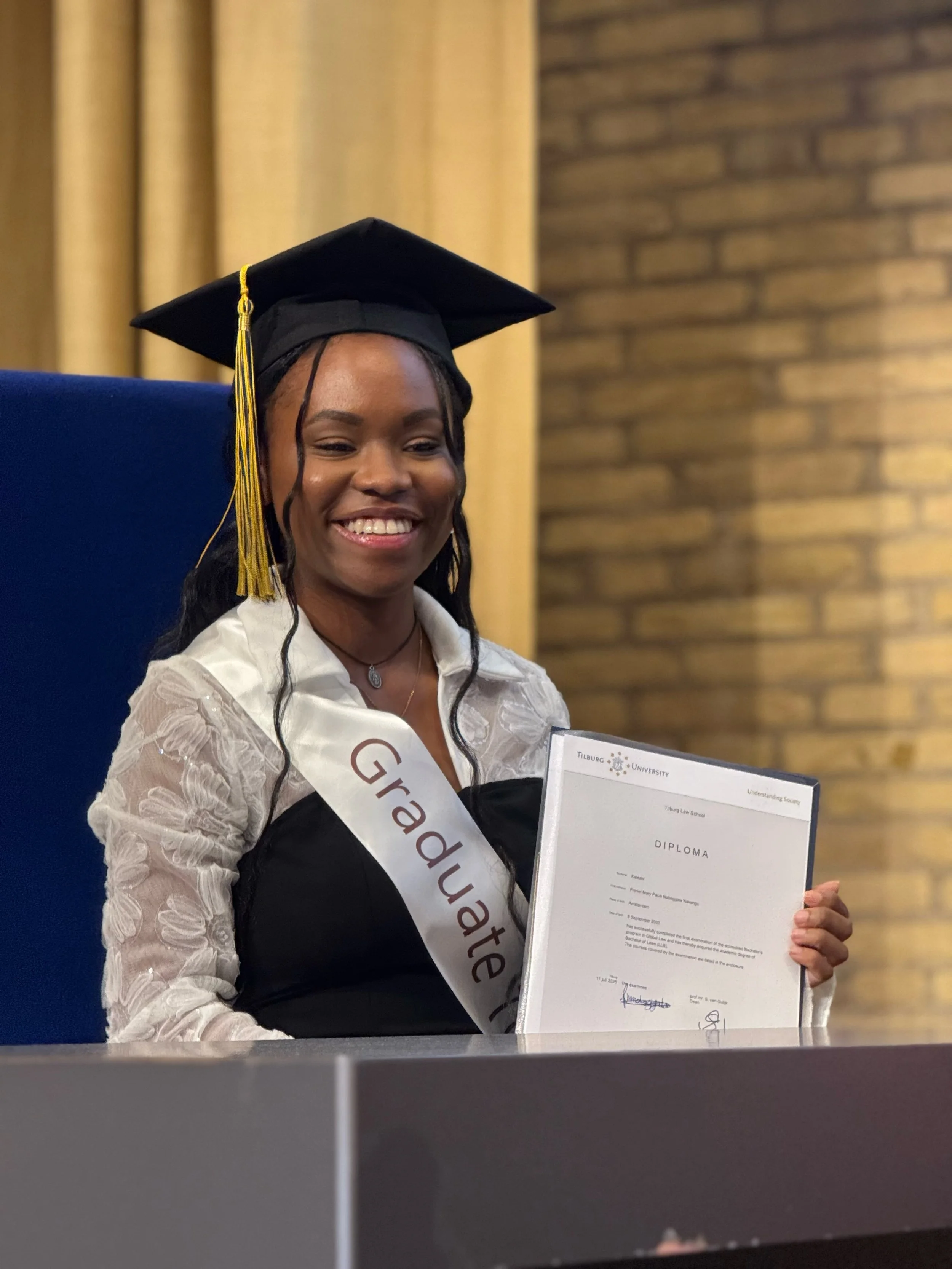 Vrouw in een afstudeerjurk, met een afstudeersjerp en een sjerp met de tekst 'Graad' op een diploma tijdens een diploma-uitreiking.