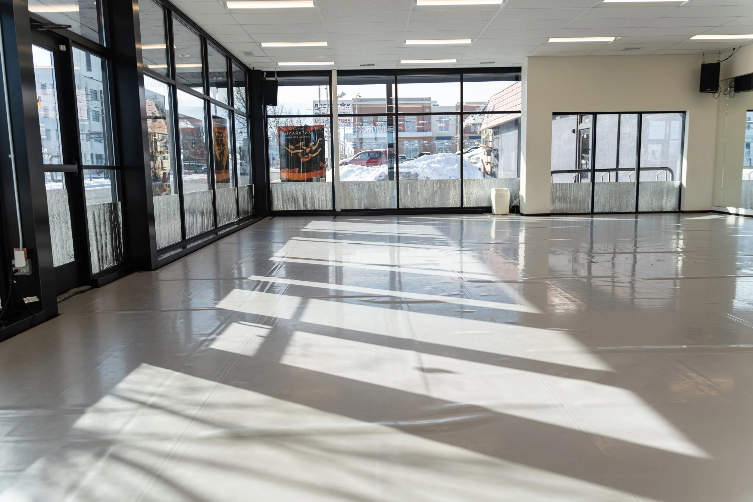 The studio on a sunny winter day. Two walls are floor-to-ceiling windows, the longest of which faces a mirror wall.