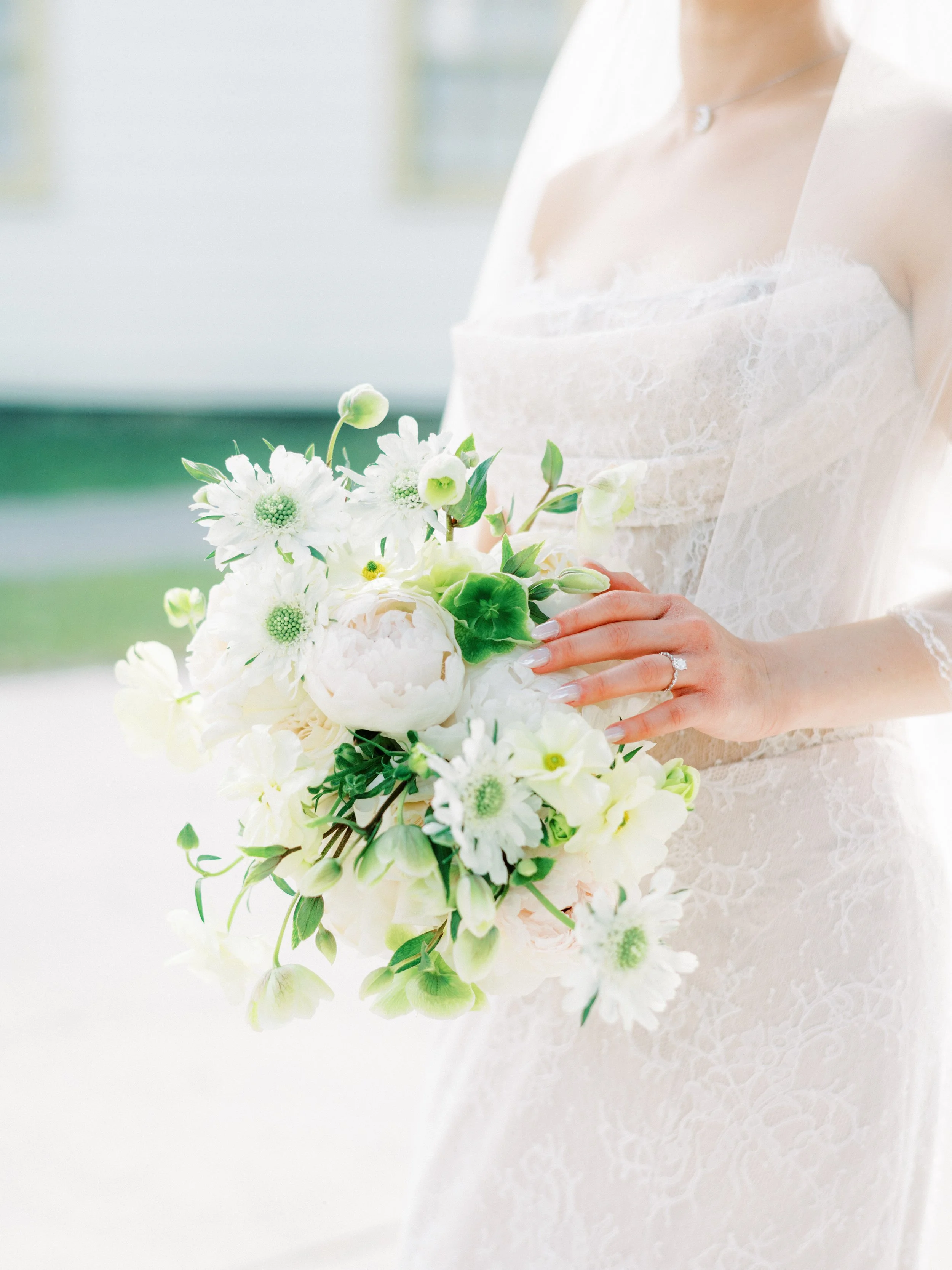 Close-up of a bride wearing a white wedding dress with lace-up back detail and matching long gloves, outdoors.