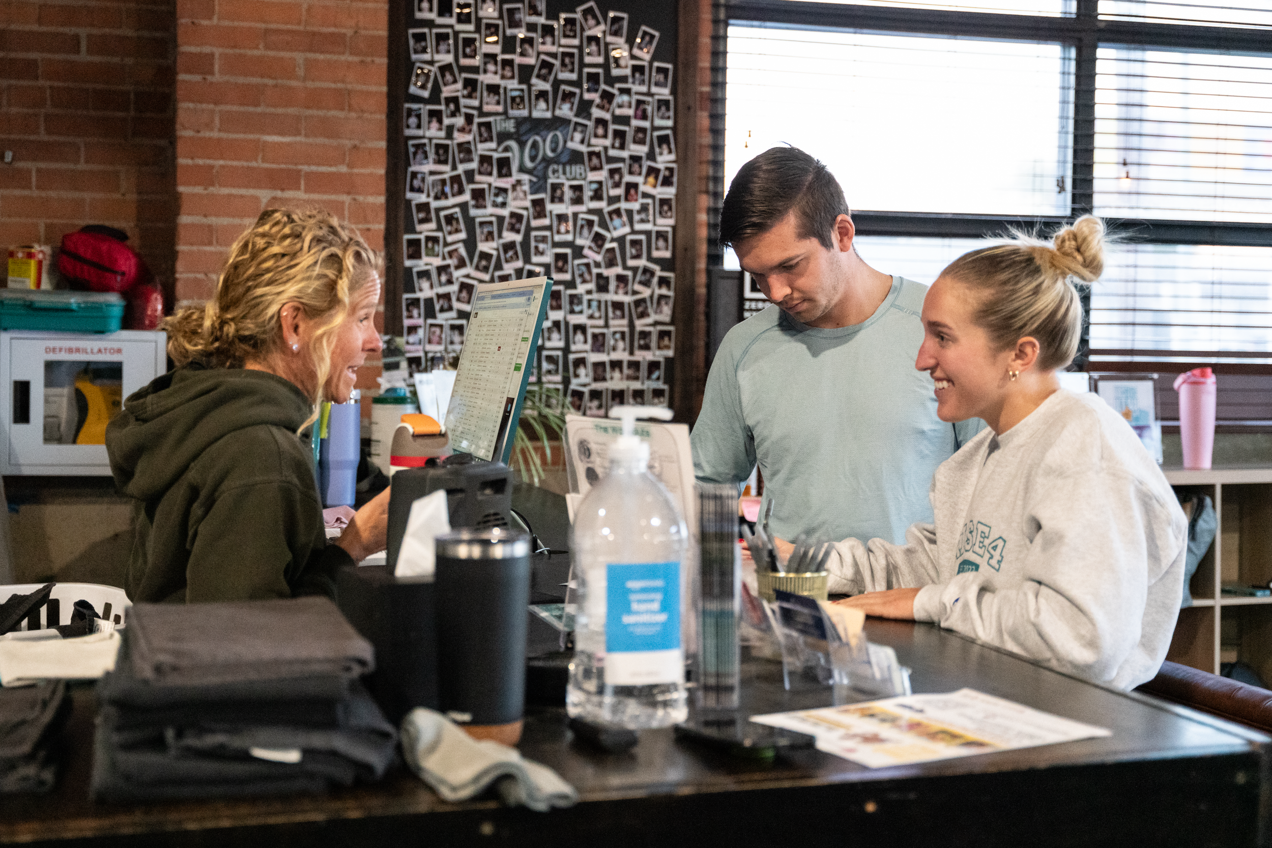 A bartender serving customers at a counter in a café or bar with a brick wall and photo collage in the background.