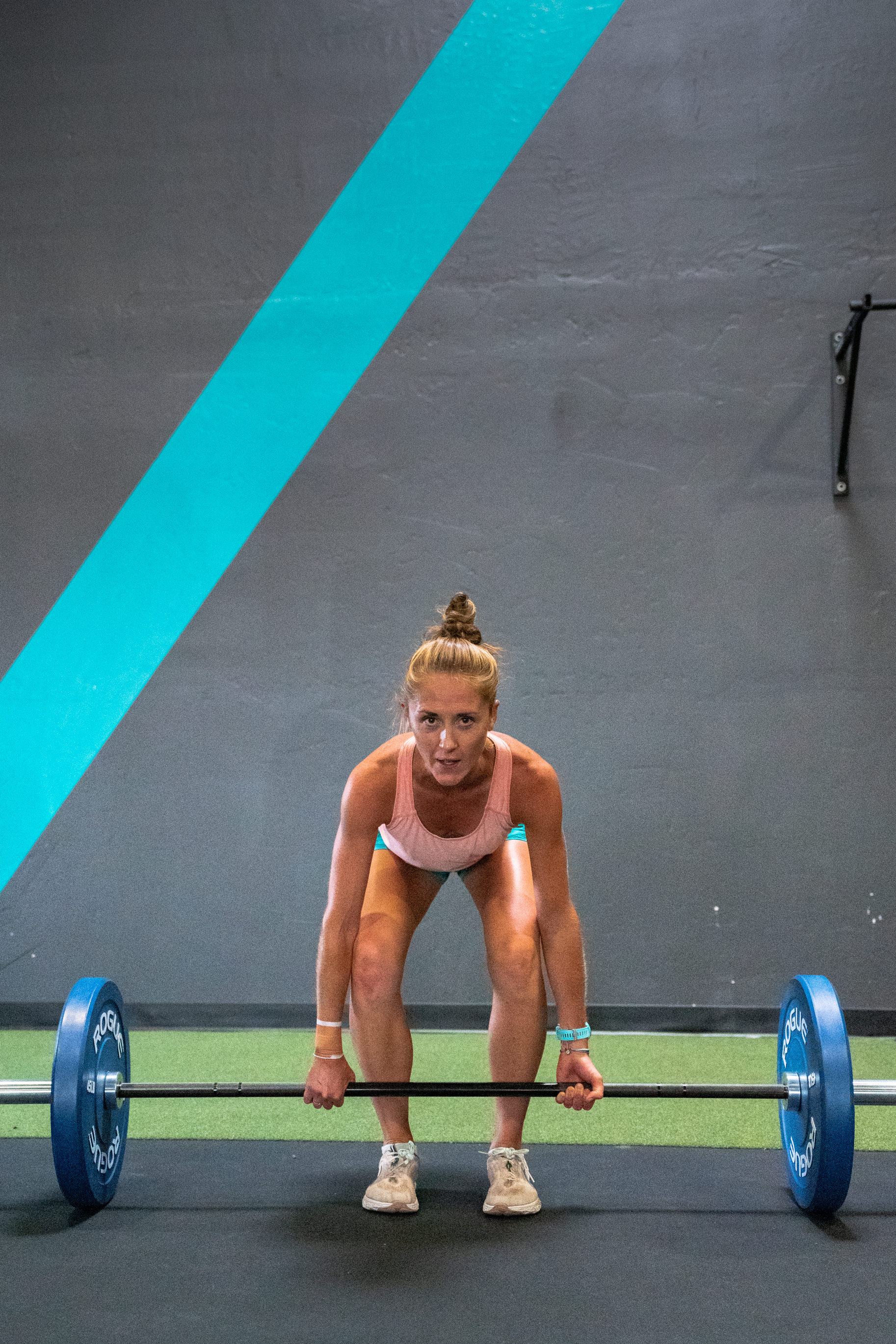 Woman in pink tank top and shorts lifting a barbell in a gym.