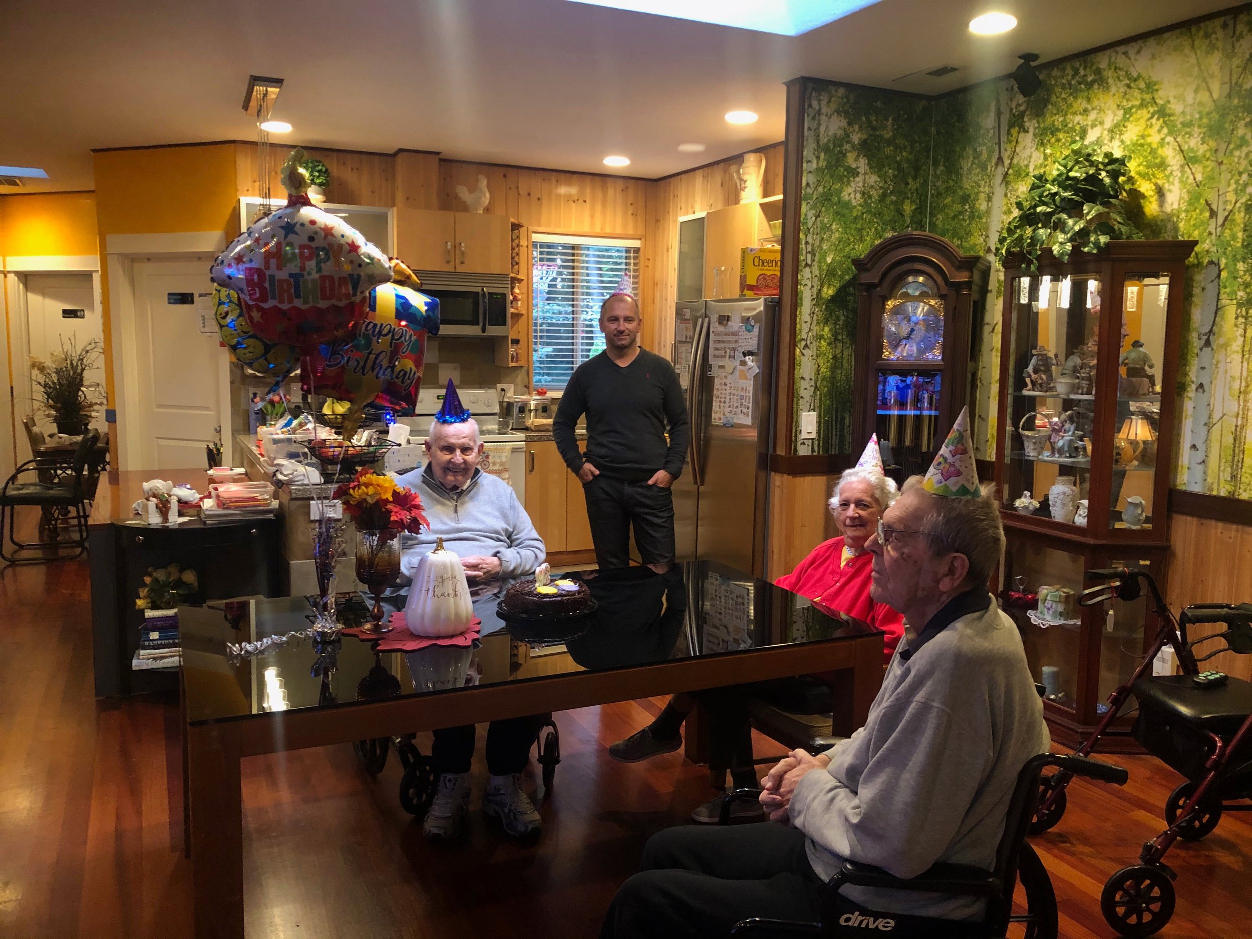 Elderly birthday celebration in a cozy kitchen with party hats, balloons, and cake