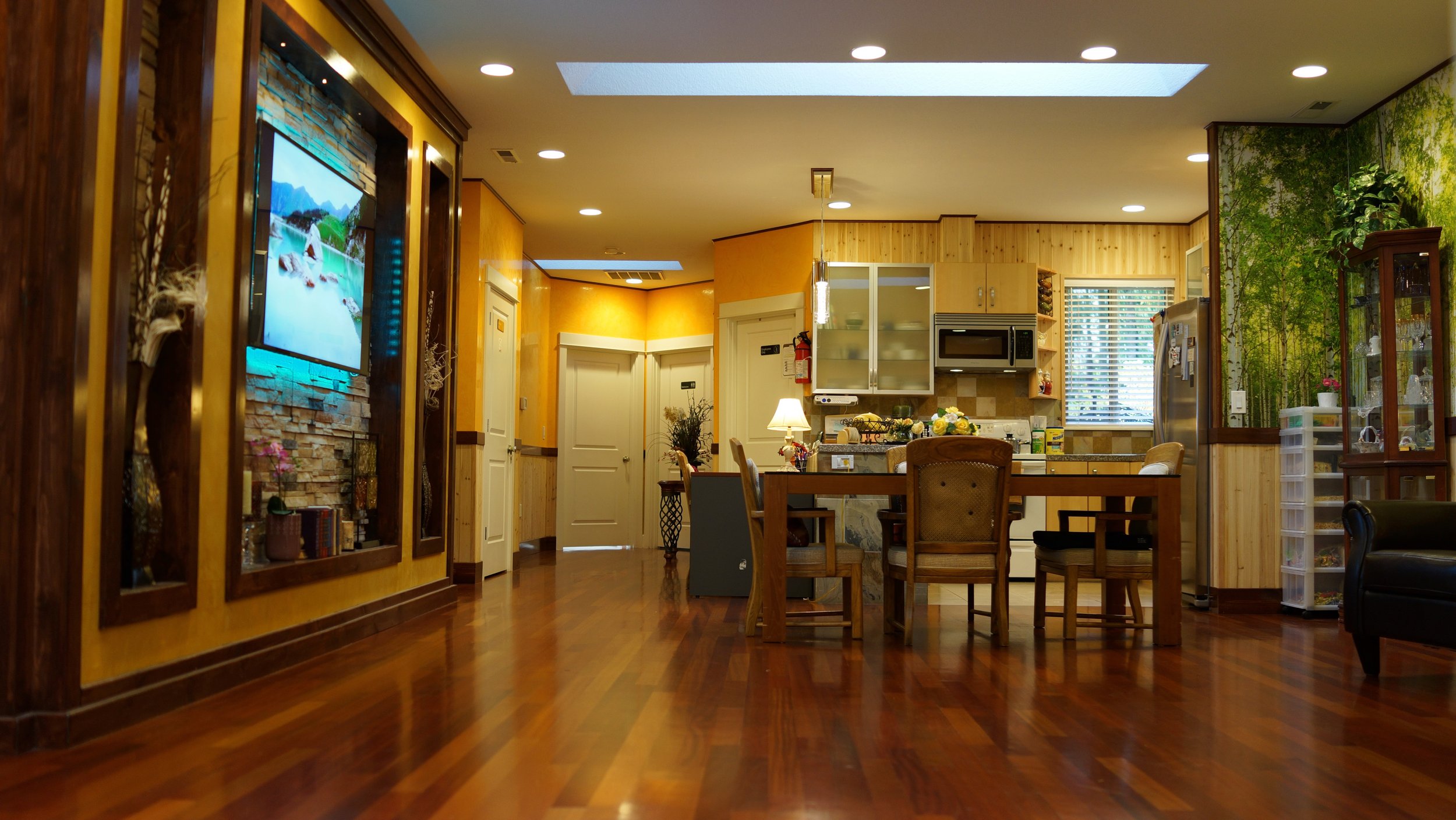 Interior of a modern kitchen and dining area with wooden floors, dining table, chairs, a refrigerator, and decorative elements on the walls.