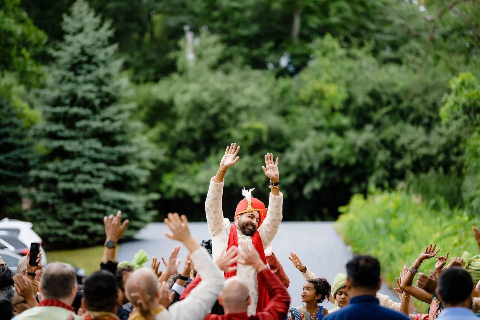The groom raises his hands in the air during the baraat ceremony at an backyard Indian wedding | Barrington IL