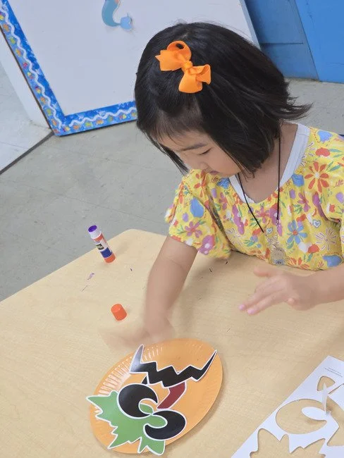 St. Matthew's Weekday School preschooler with an orange bow working on a fall craft at the classroom table