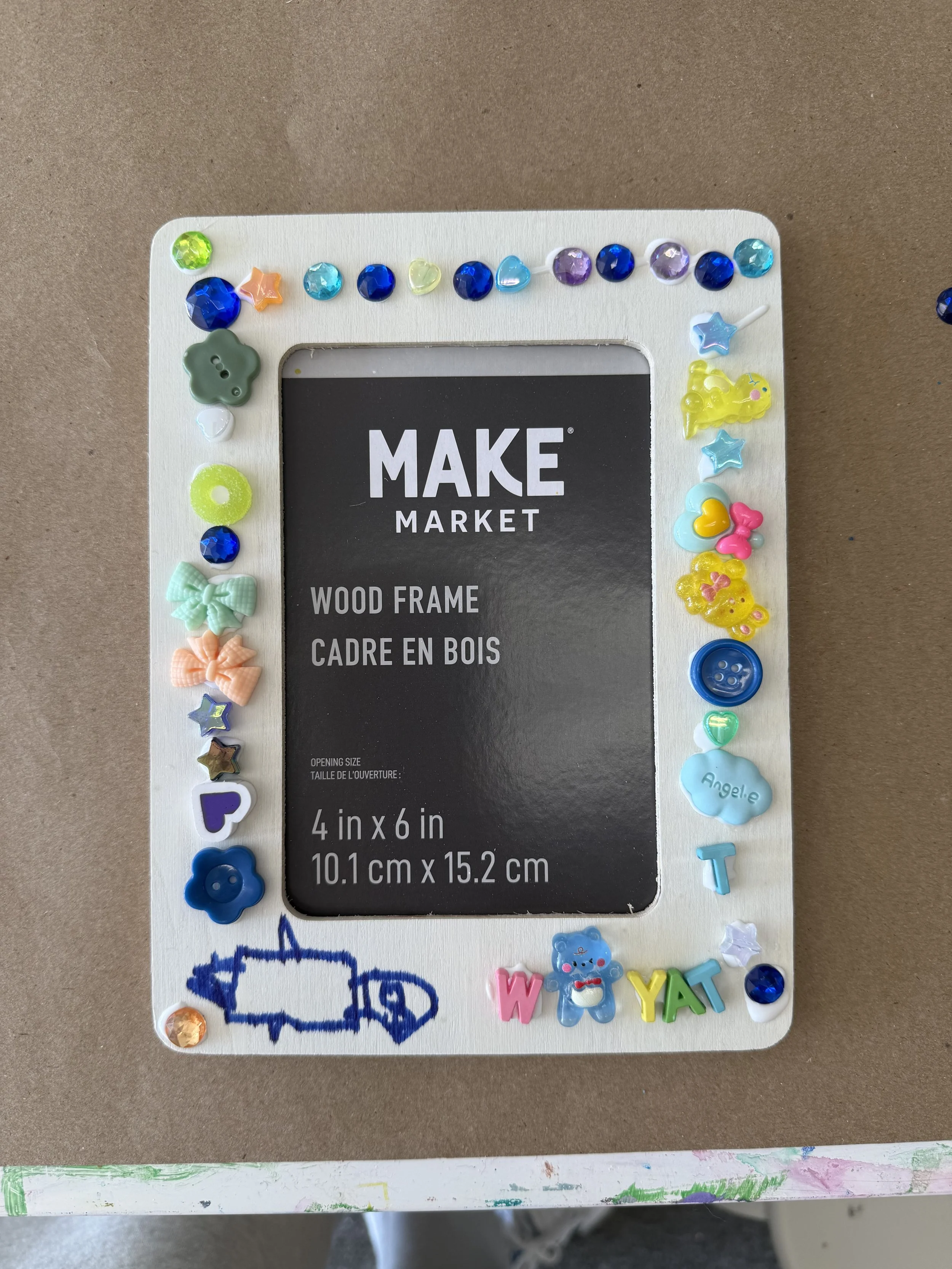 A craft workspace with paintbrushes, watercolor paints, scissors, sequins, pink flower-shaped embellishments, and multicolored feathers.