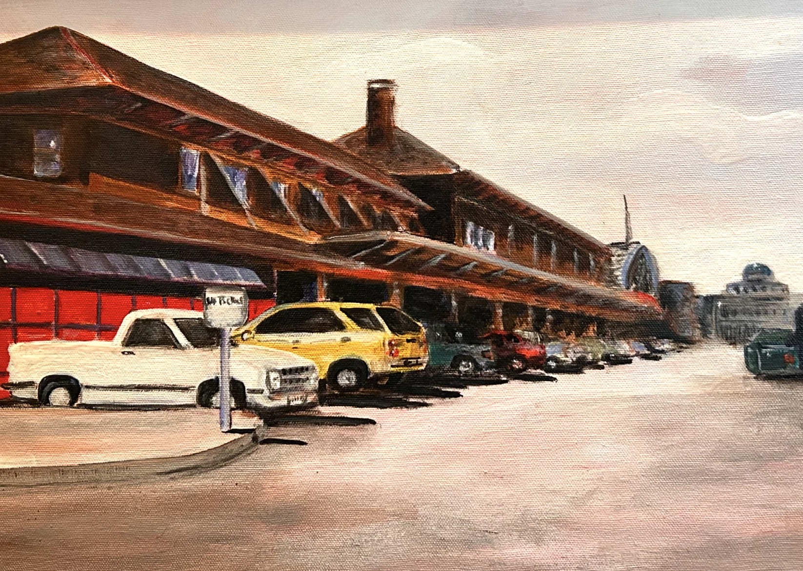 A painting of downtown Des Moines, Iowa by Jean Shelton. The painting shows several cars of various colors parked in front of a brown train depot. A grey government building is located at the end of the road.