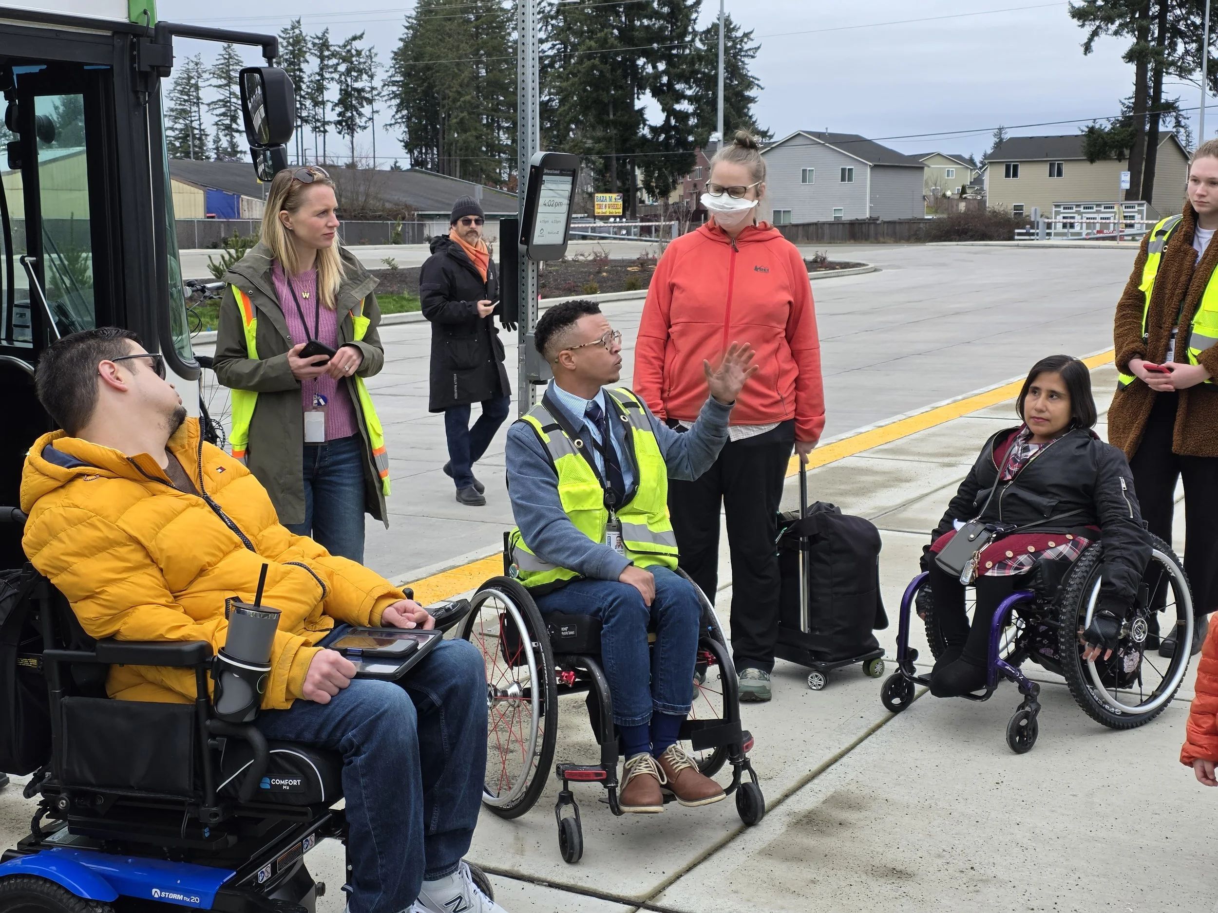 A group of people with different disabilities talking to each other at a bus transfer station.