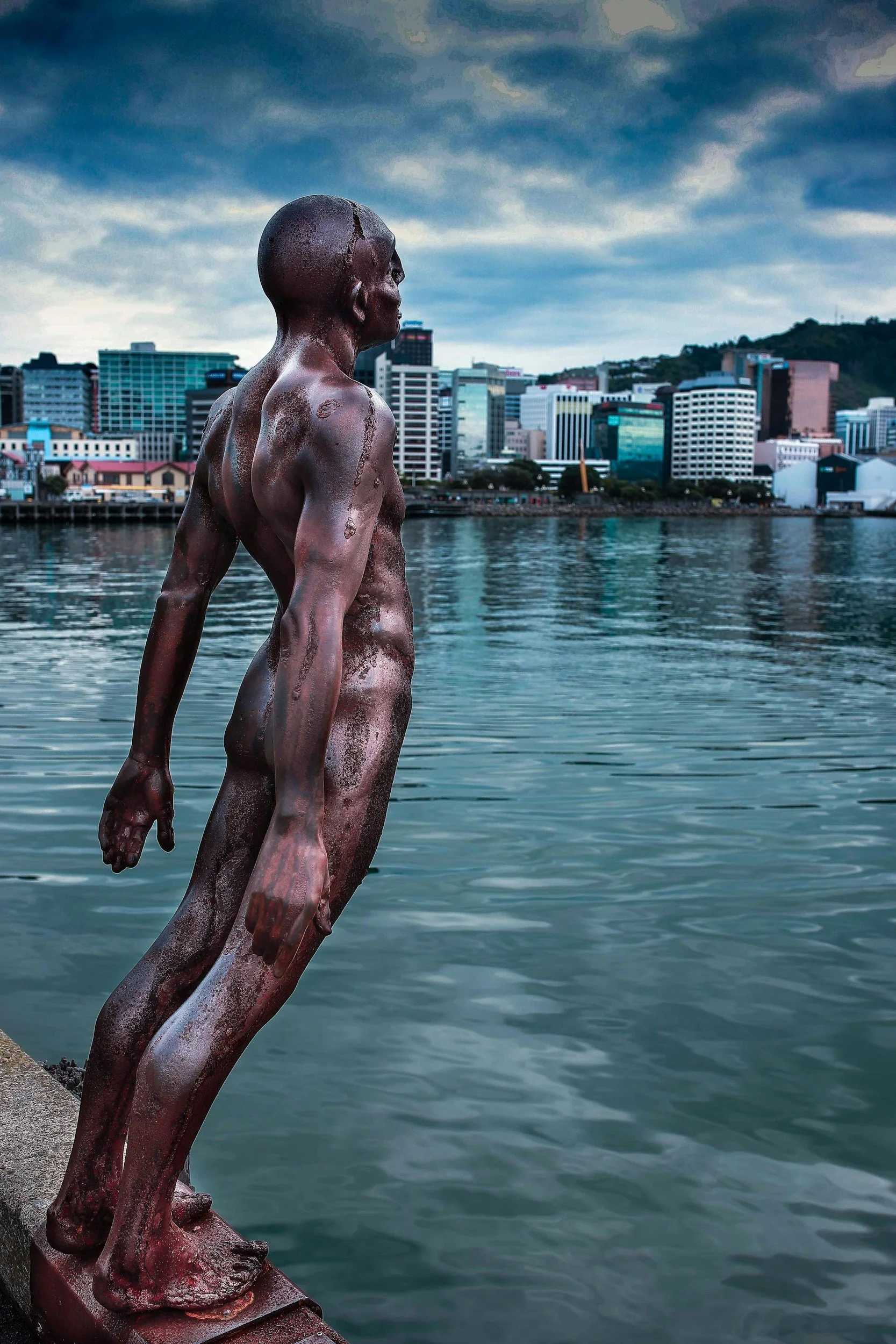Bronze sculpture of a figure rising from the calm water of Wellington's harbour, city skyline behind