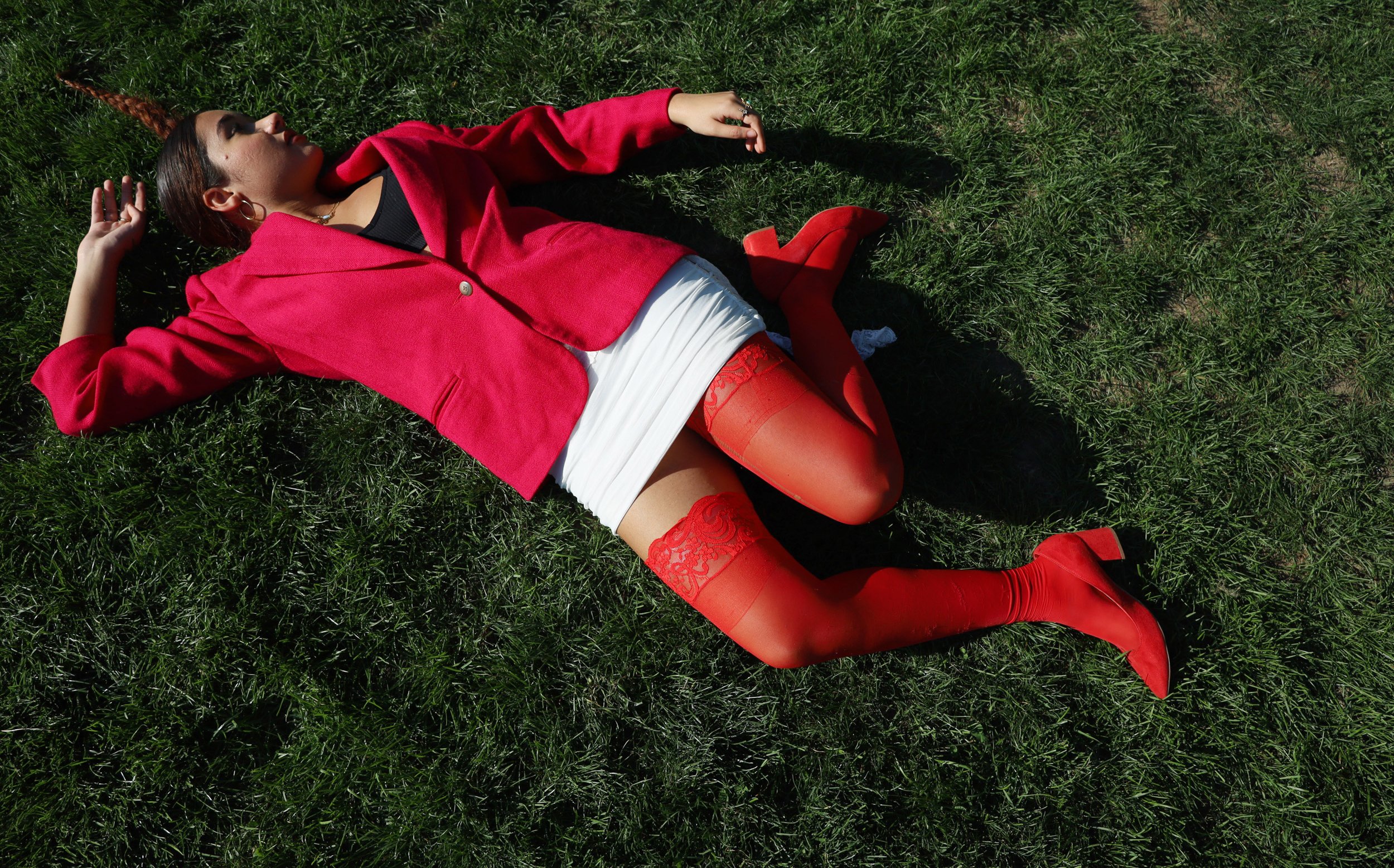 BOSTON, MA--10.4.25--Abigail Rosario lies in the grass at Amory Park. She wears a bright red blazer, stockings and heels. 