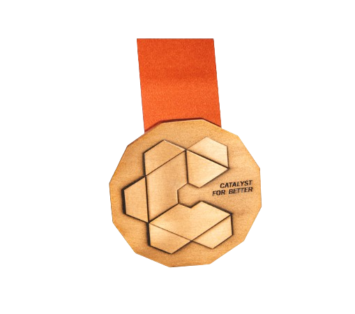 A wooden coaster with a hexagonal geometric design and the text 'CATALYST FOR BETTER'. It is placed on an orange and beige surface.