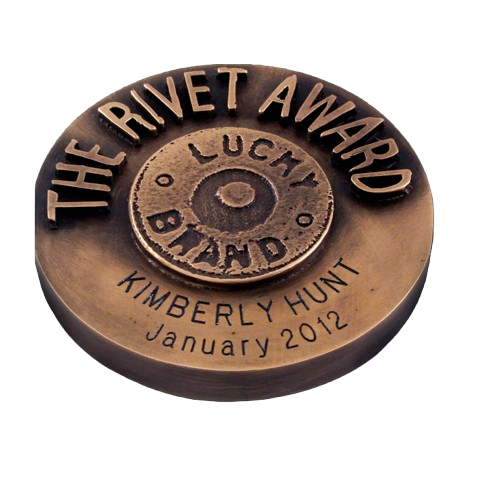 A bronze award medal with the inscription "The Rivet Award" and details "Lucia Brand" and "Kimberly Hunt, January 2012" engraved on it.