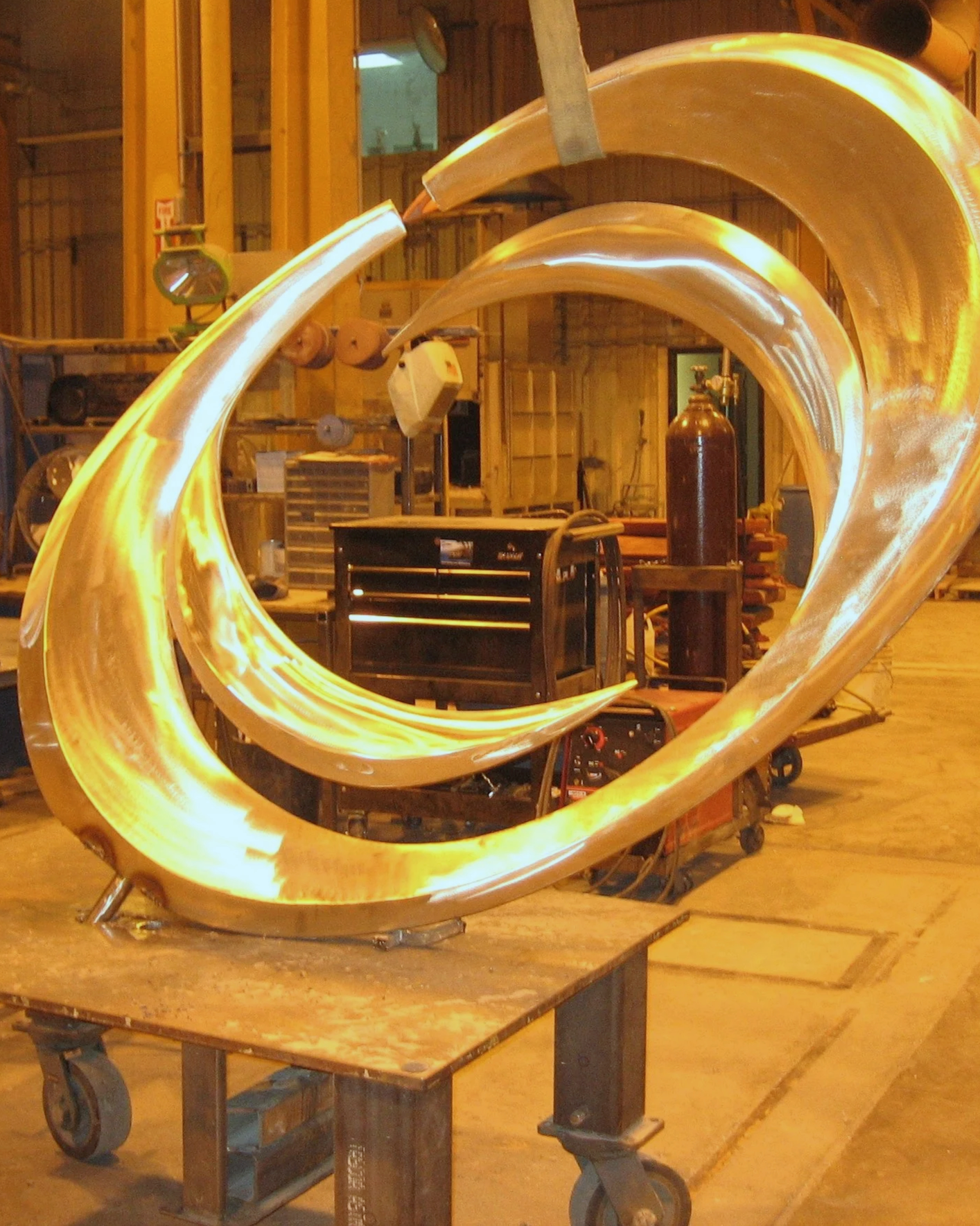 A large illuminated metal 'C' shaped sculpture in a workshop.