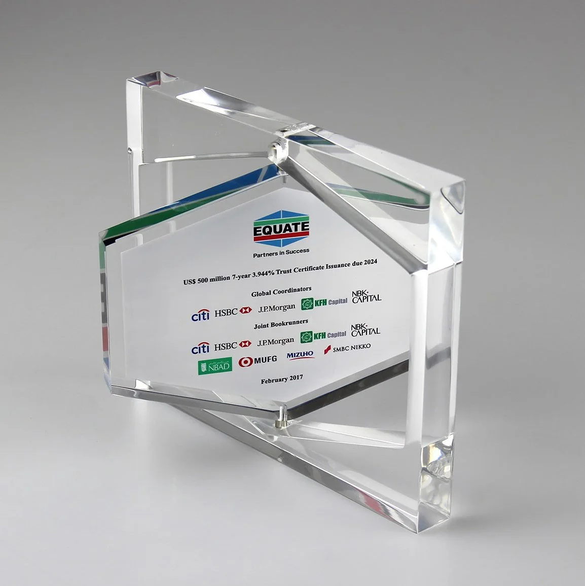 A clear glass award with a rectangular shape, featuring colorful logos and text engraved on it, standing on a flat surface.