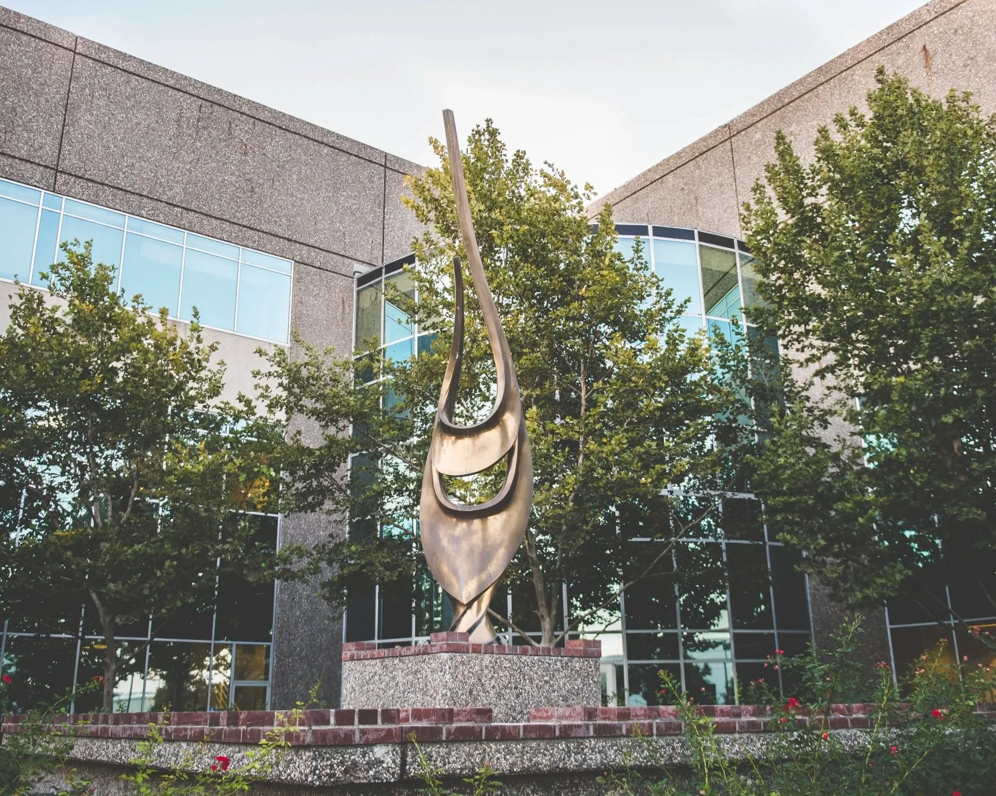 Modern glass building with trees and a metal abstract sculpture in front.