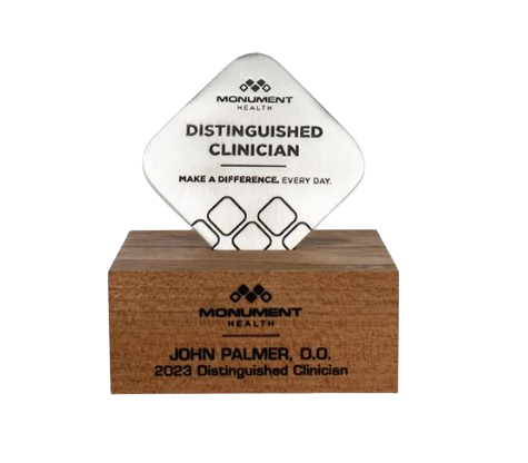 A plaque with the Monument Health logo that reads, "Distinguished Clinician. Make a Difference Every Day," placed on a wooden base that has a nameplate for John Palmer, D.O., 2023 Distinguished Clinician.