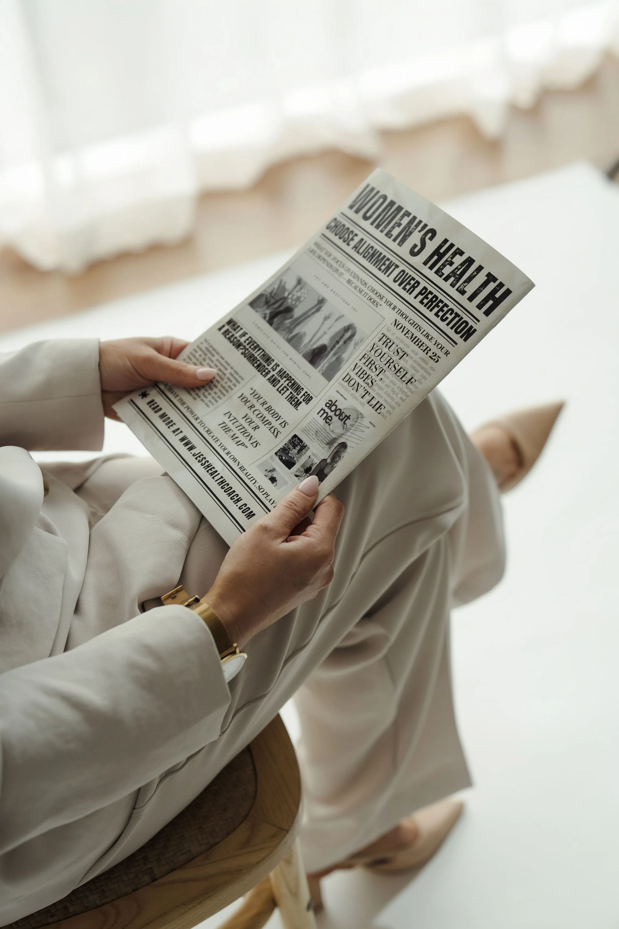Woman in a cream suit sitting and reading a women's health newspaper