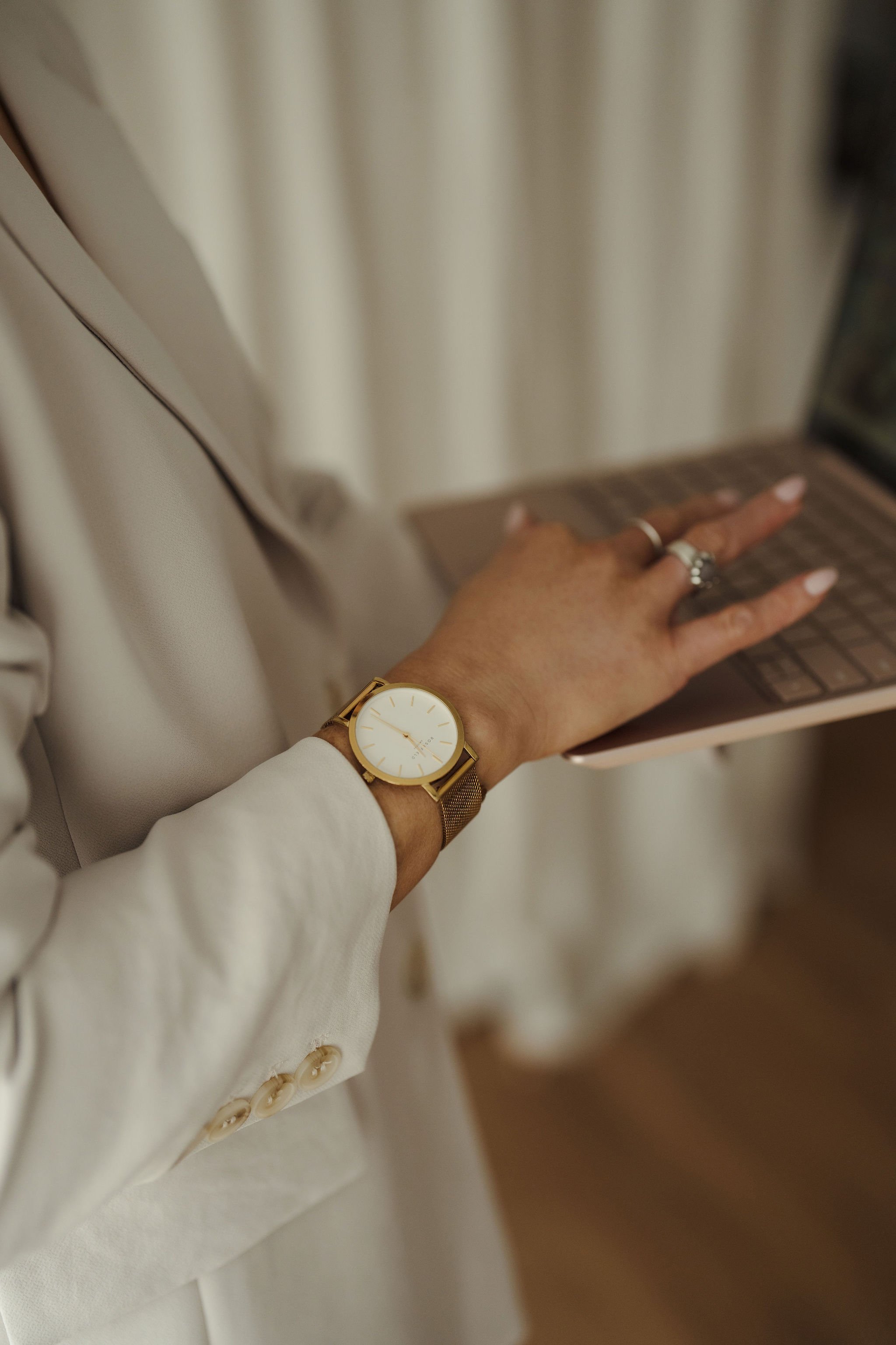 Close-up of a woman's hands typing on a laptop, wearing a watch and rings