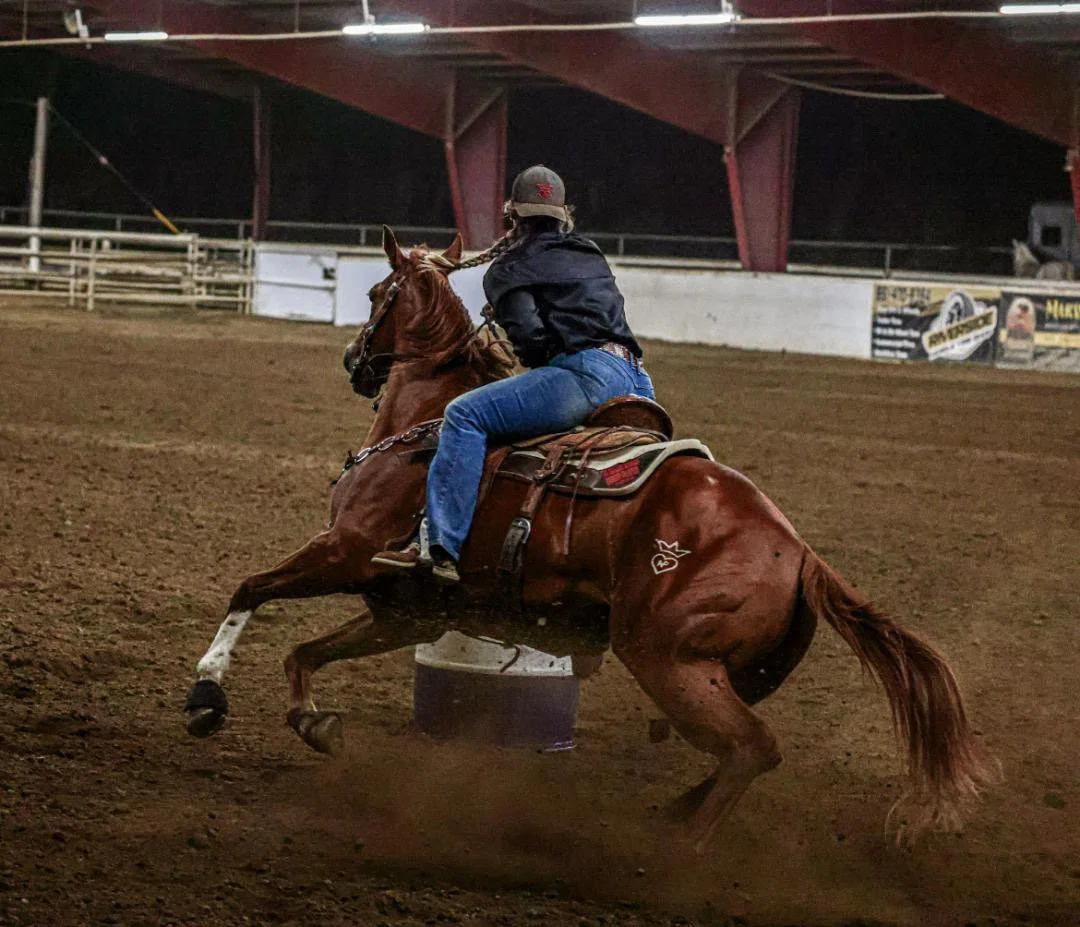 A person riding a horse around a barrel in an indoor arena during a rodeo event.