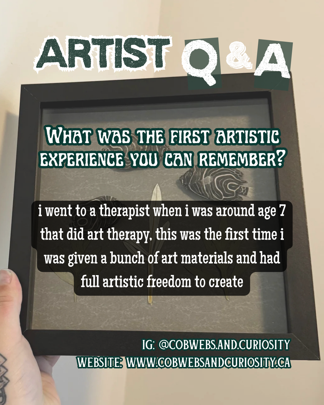 A framed display with text and artwork. The top text says 'ARTIST Q & A'. The main question asks, 'What was the first artistic experience you can remember?' A person's hand is holding the frame, showing part of their arm and a tattoo. The background 