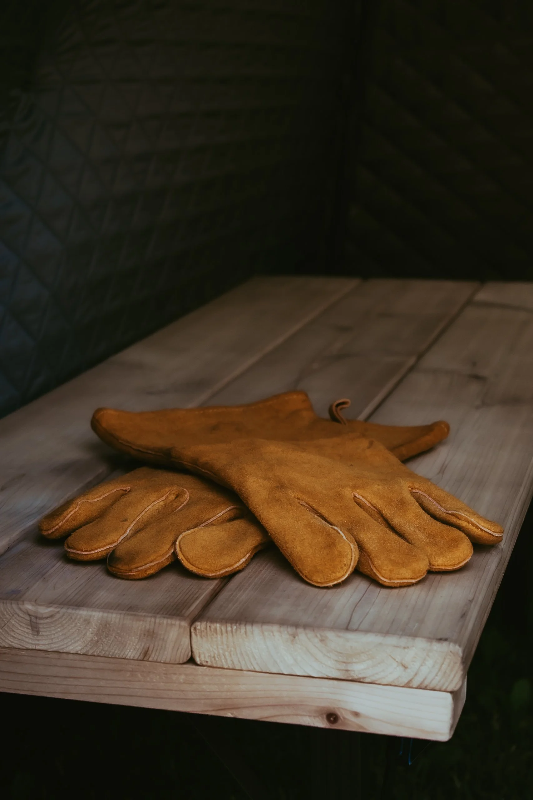 A pair of tan leather gloves resting on a wooden surface.