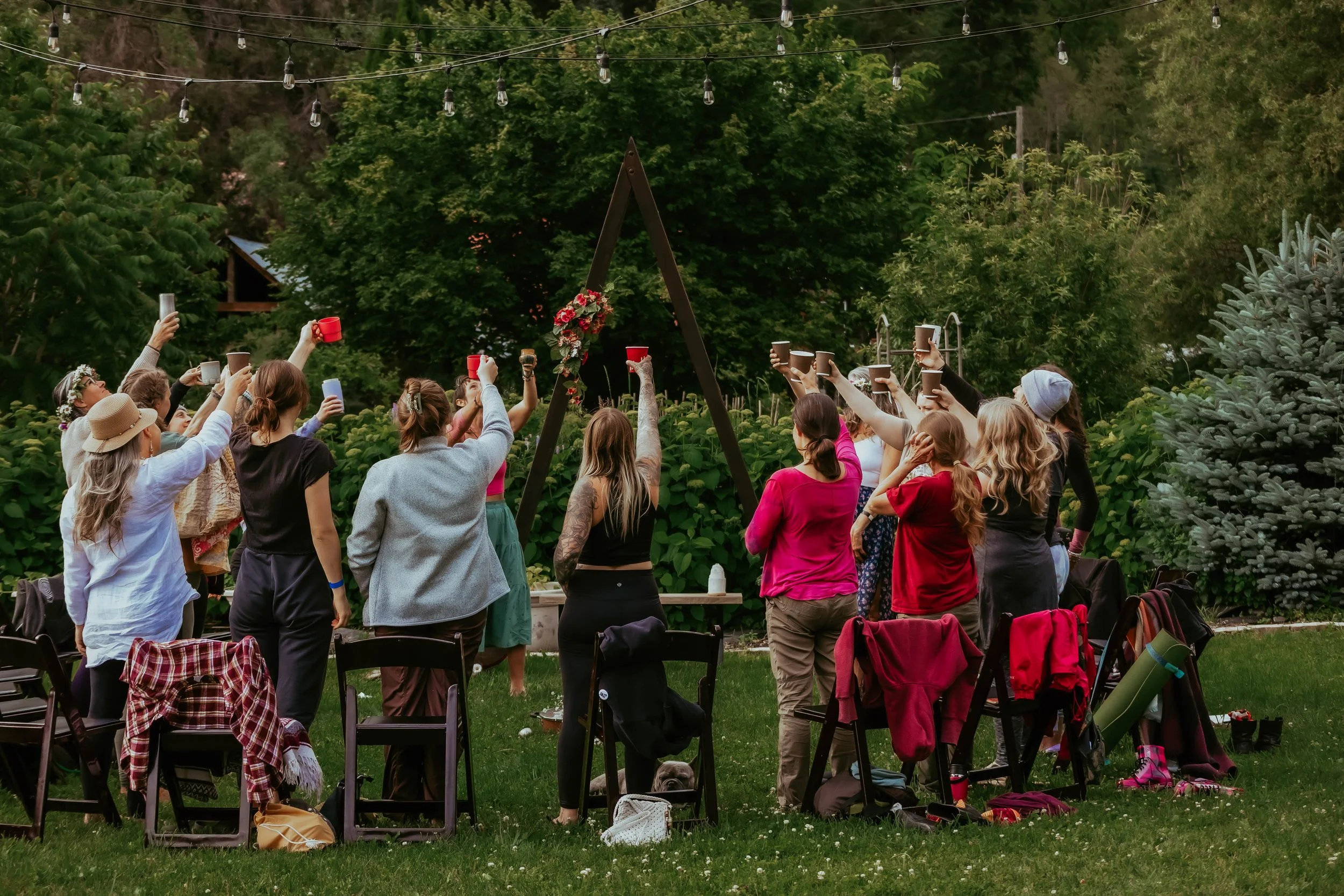 (photographed from behind) women gatherer in a circle holding up cacao with a forest background and wooden mountain altar