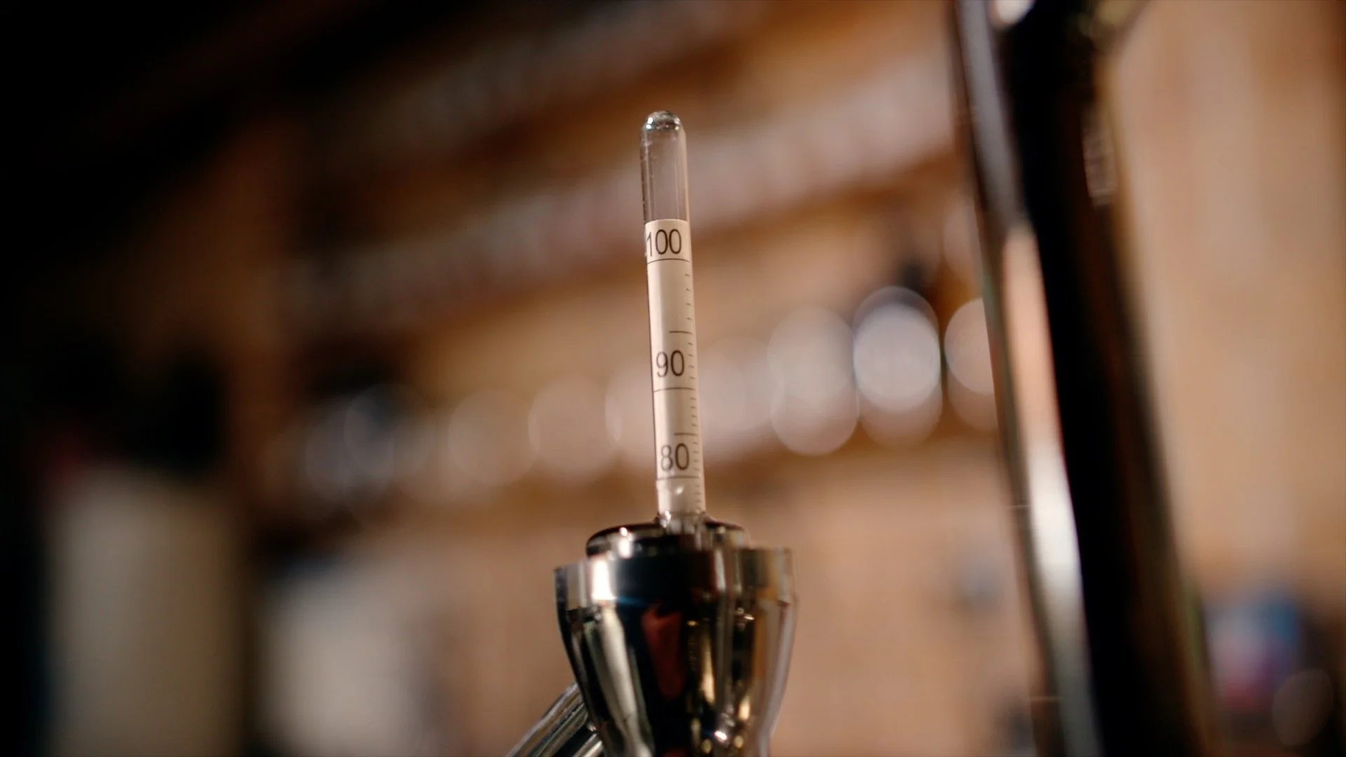 A close-up of a thermometer at the top of a parrot on a still, in a distillery.