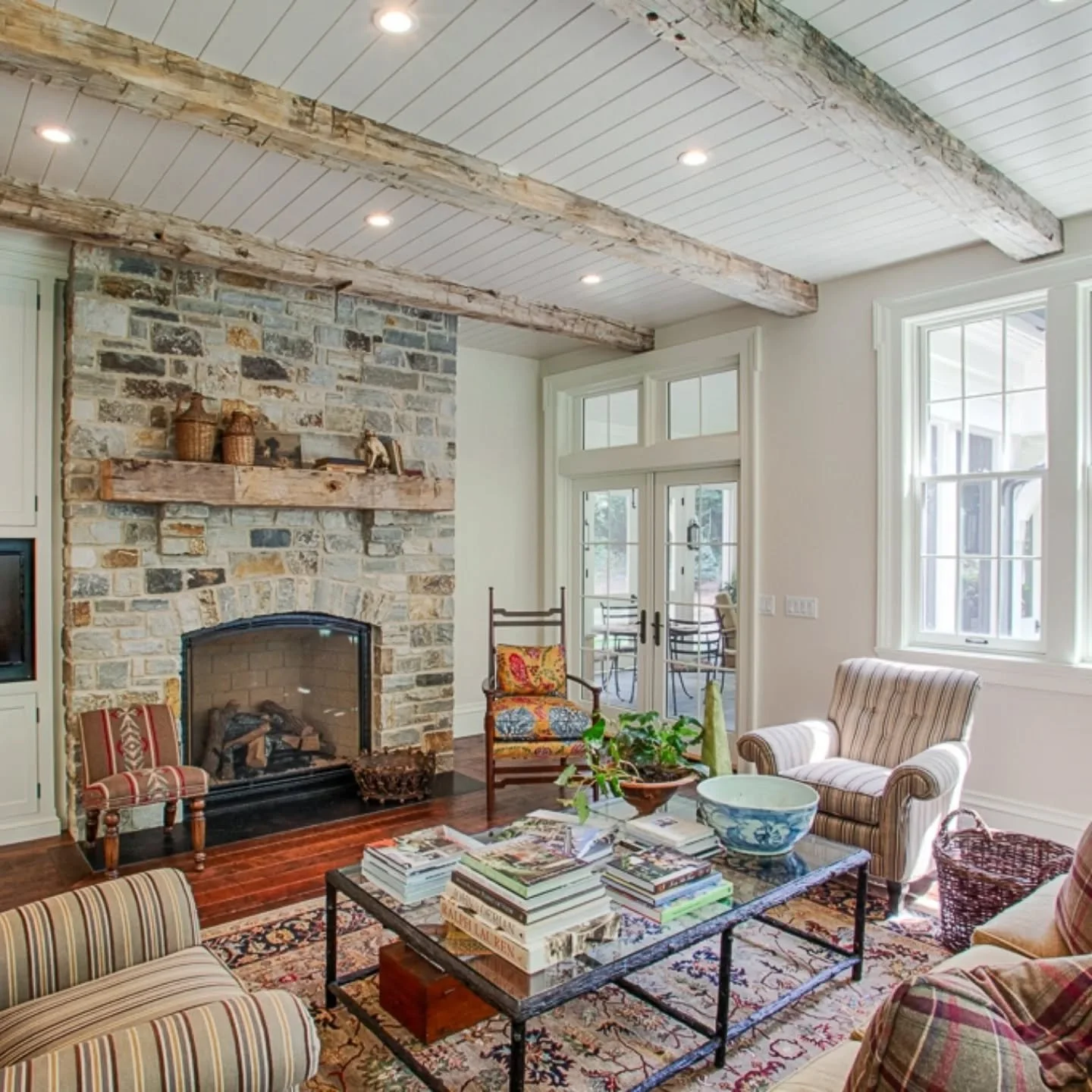 When designing a space, it's important to think about how it will be lived in. This sunroom, just off the kitchen, is the perfect place to begin your day with a cup of coffee or end it by the fire. A warm stone fireplace, reclaimed timbers, and a rus
