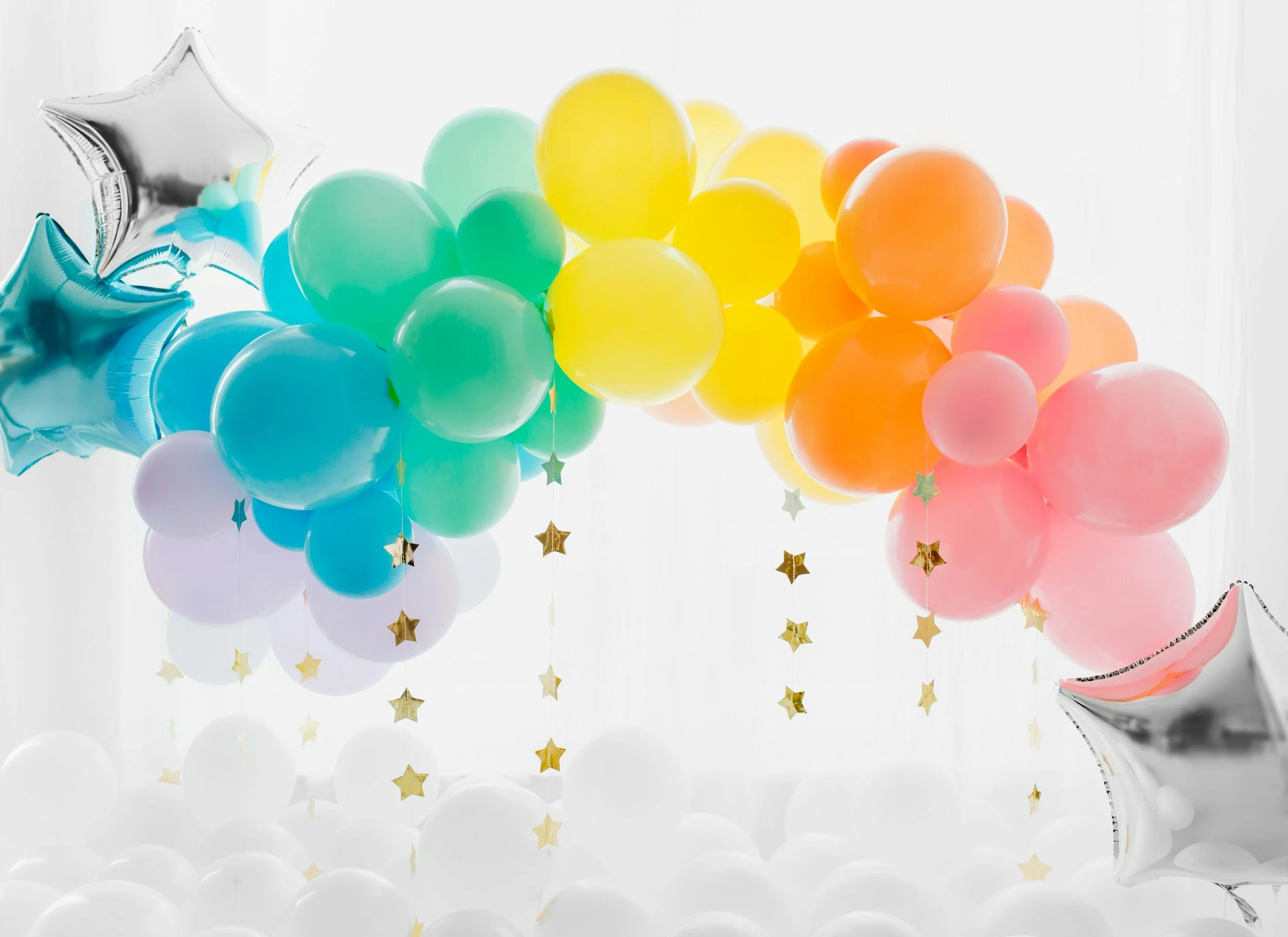 Colorful balloons in various shades of green, yellow, orange, pink, blue, and purple with star-shaped metallic hanging decorations, set against a white background.