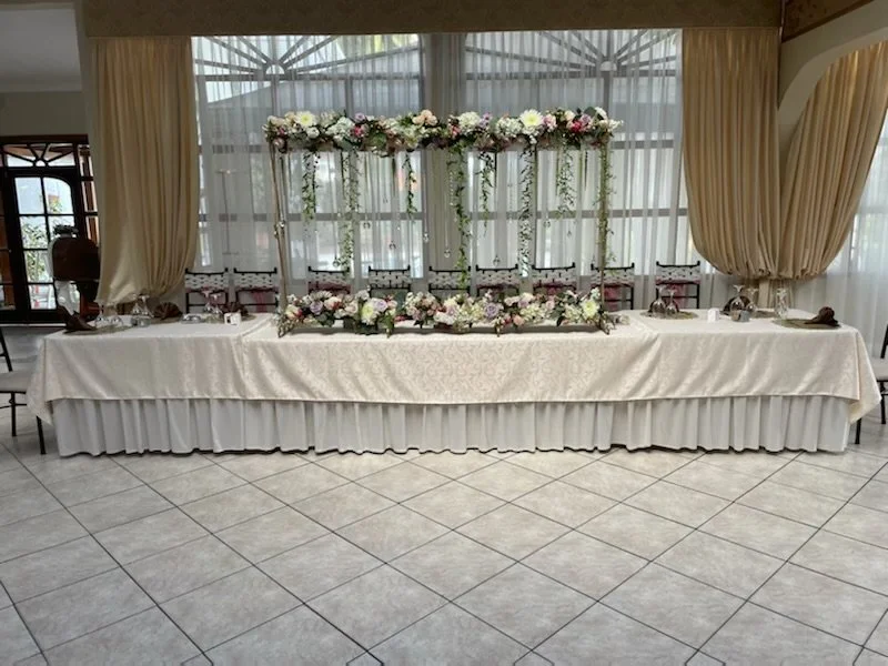 Wedding reception table with floral arrangements and a decorative backdrop of flowers and greenery.