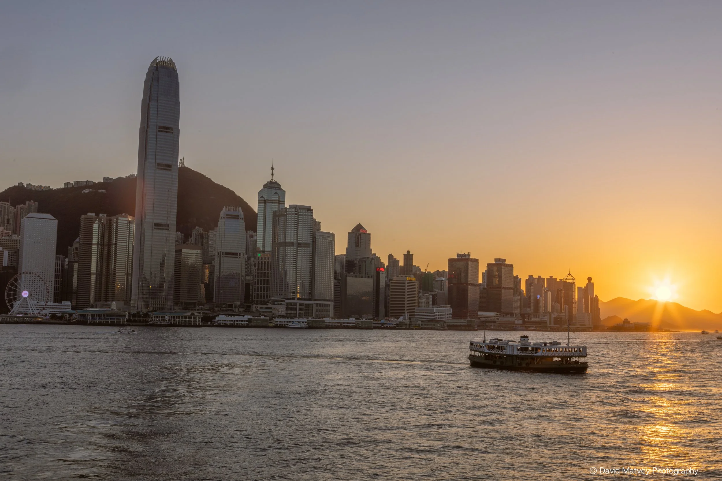 Sunset over the Hong Kong skyline with high-rise buildings and a ferry on the water