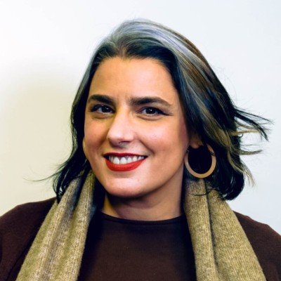 Woman with dark hair and highlights, wearing hoop earrings and a brown top, smiling.