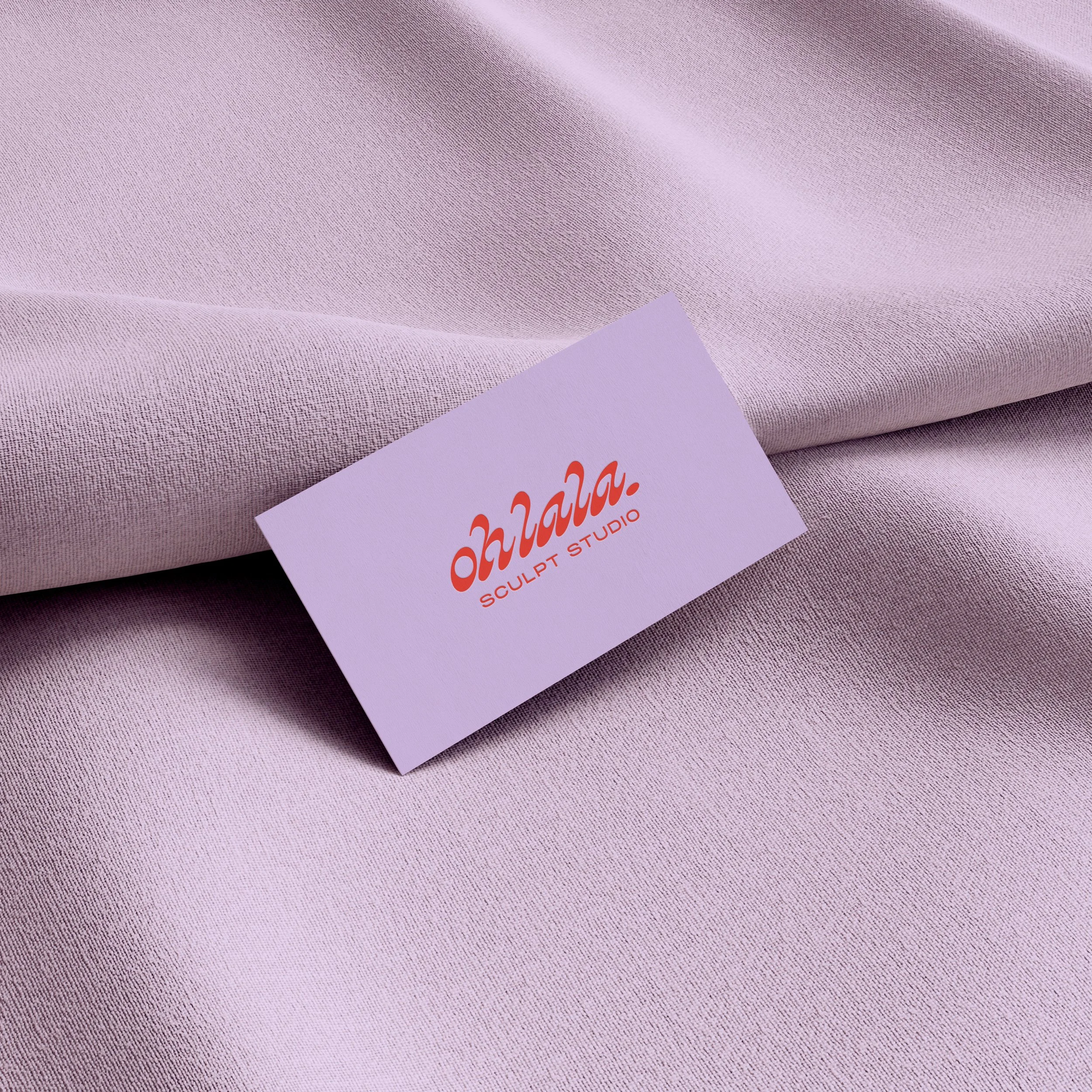 Un tissu couleur parme pâle avec une carte de visite portant le logo orange 'Ohlala' et la base line 'SCULPT STUDIO'.