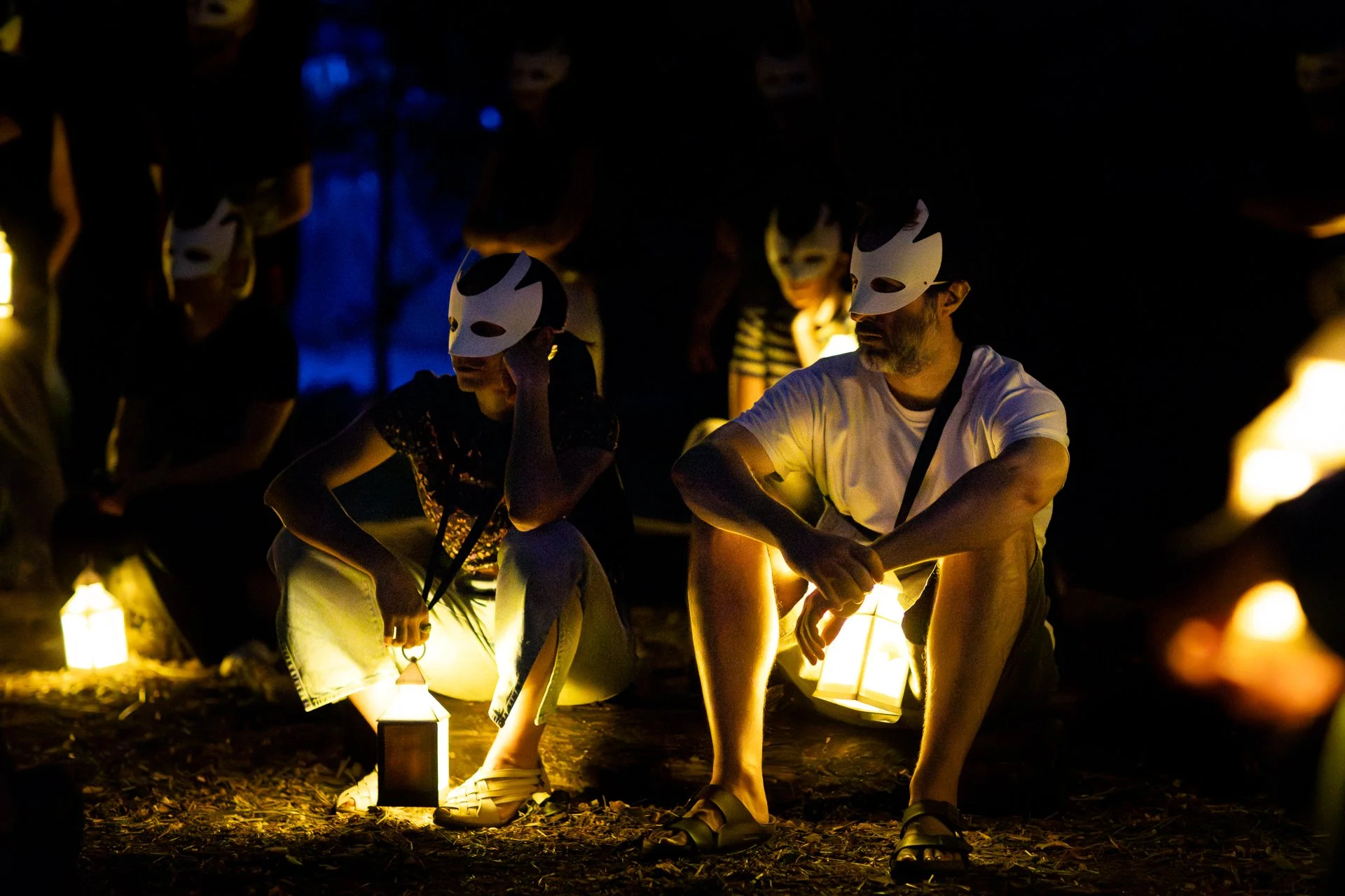 Gli spettatori sono seduti ad osservare la scena davanti a loro. Indossano una maschera bianca che gli copre parzialmente il volto e ognuno ha una lanterna.

Foto di Davide Aiello.