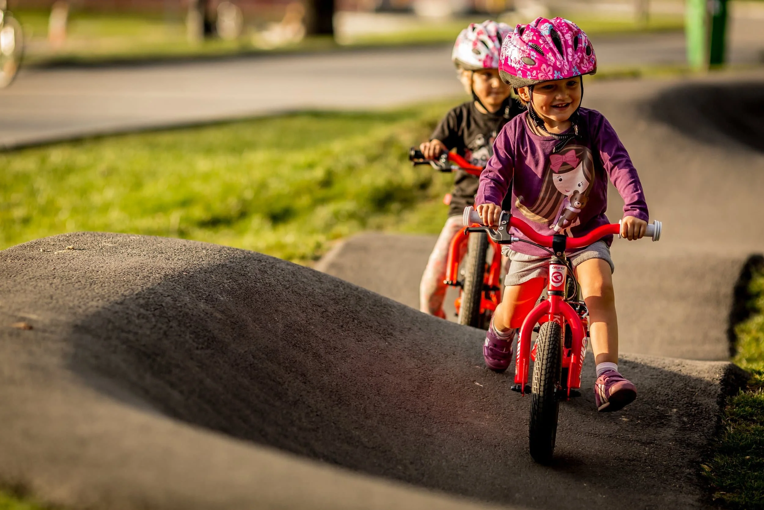 Deux enfants portant des casques, faisant du vélo sur un parcours avec des bosses.