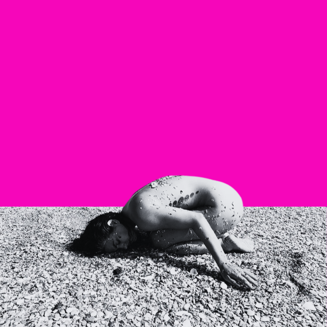 A woman is curled up on a pebbled beach with her head resting on the ground, partially covered in water droplets, against a vibrant pink background.
