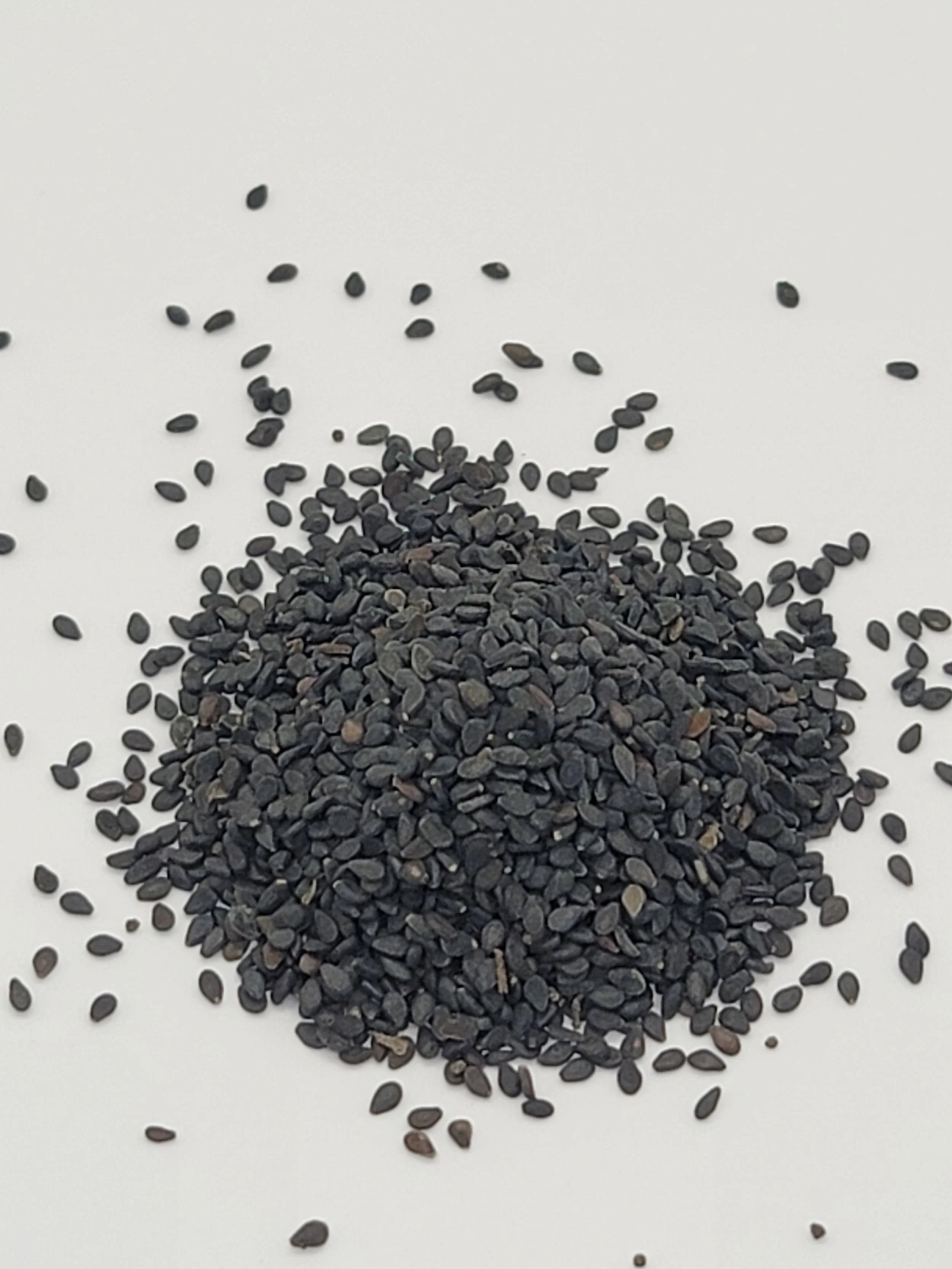 Black sesame seeds scattered on white surface.