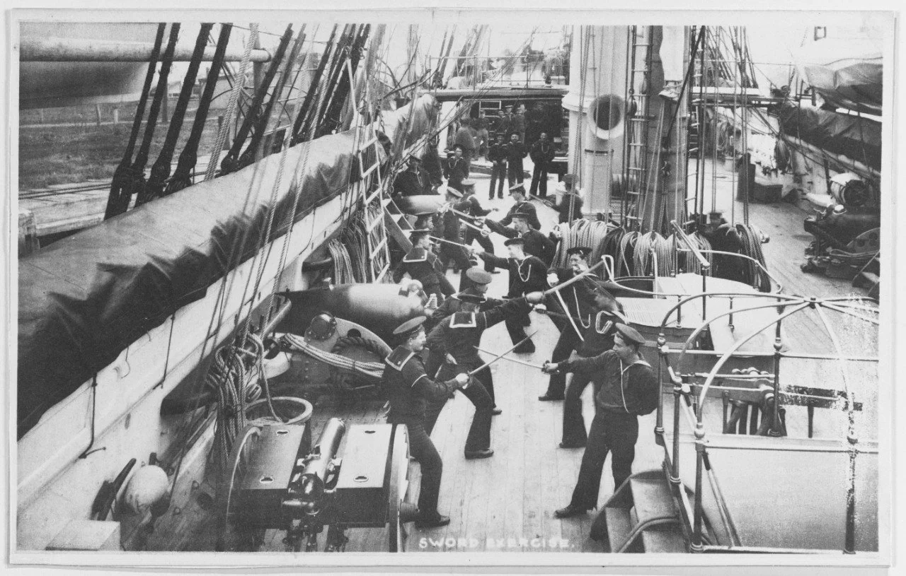 Photo Above: Sailors aboard Enterprise circa 1890 drill with cutlasses.  They are standing beside the ship’s 9-Inch Dahlgrens on the main deck.  Naval History and Heritage Command Photo NH 54205.