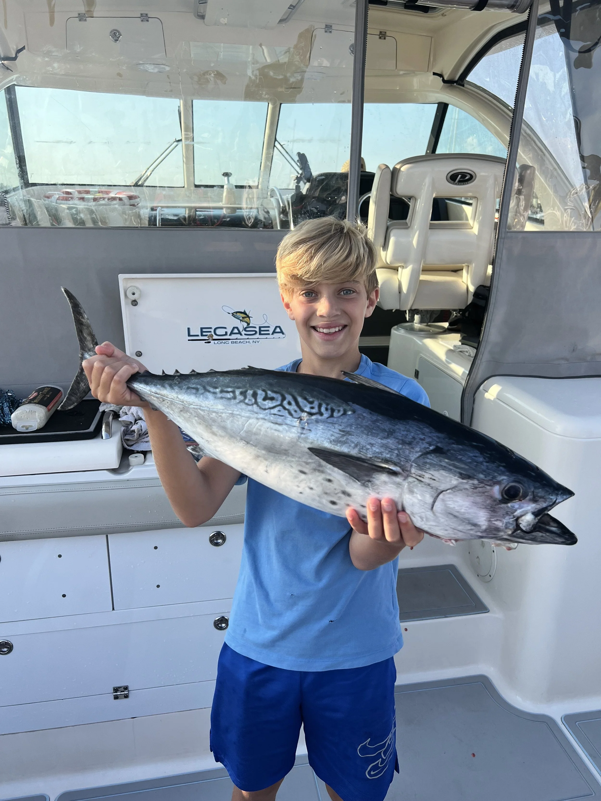 A young boy with blond hair smiling and holding a large fish on a boat.